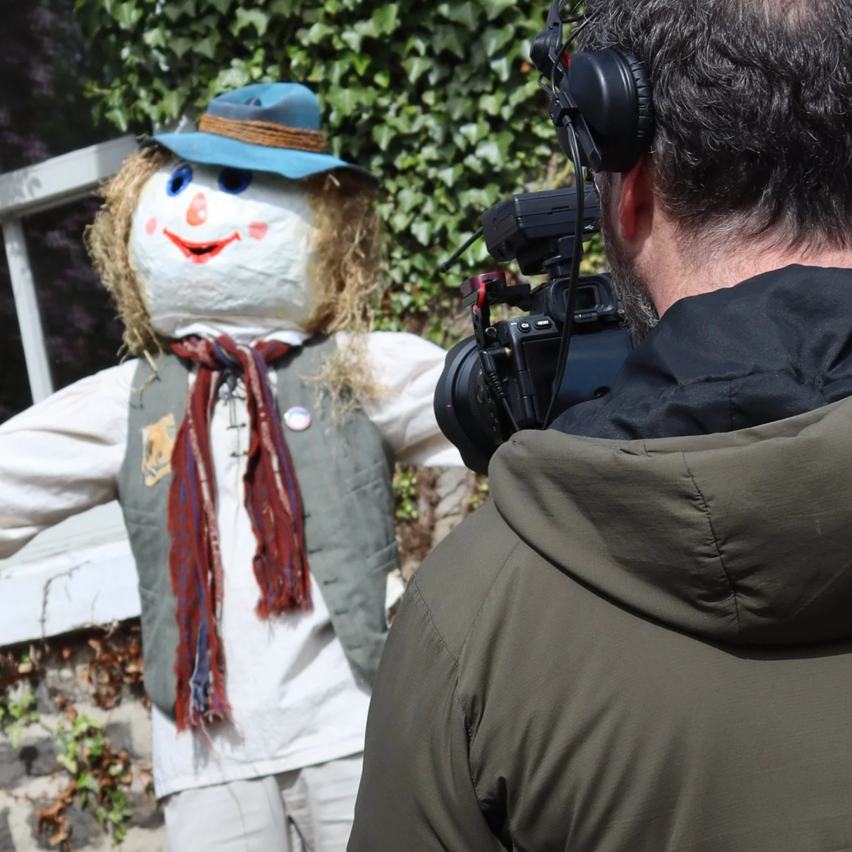 Photographer capturing a scarecrow dressed as a hiker in an outdoor setting with green ivy in the background.