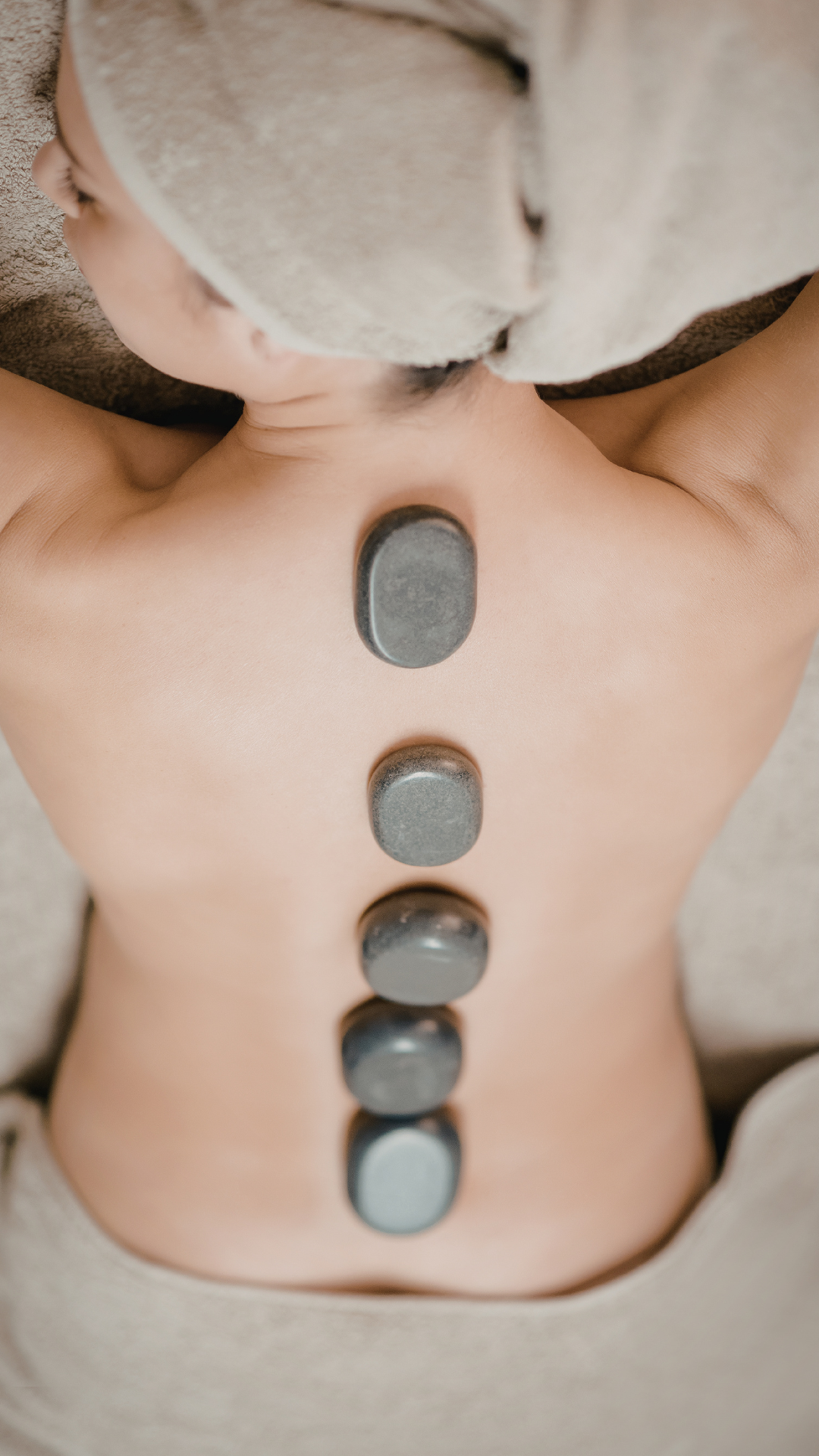 A person lying face down receiving hot stone therapy, with five smooth, oval-shaped stones placed along their back.