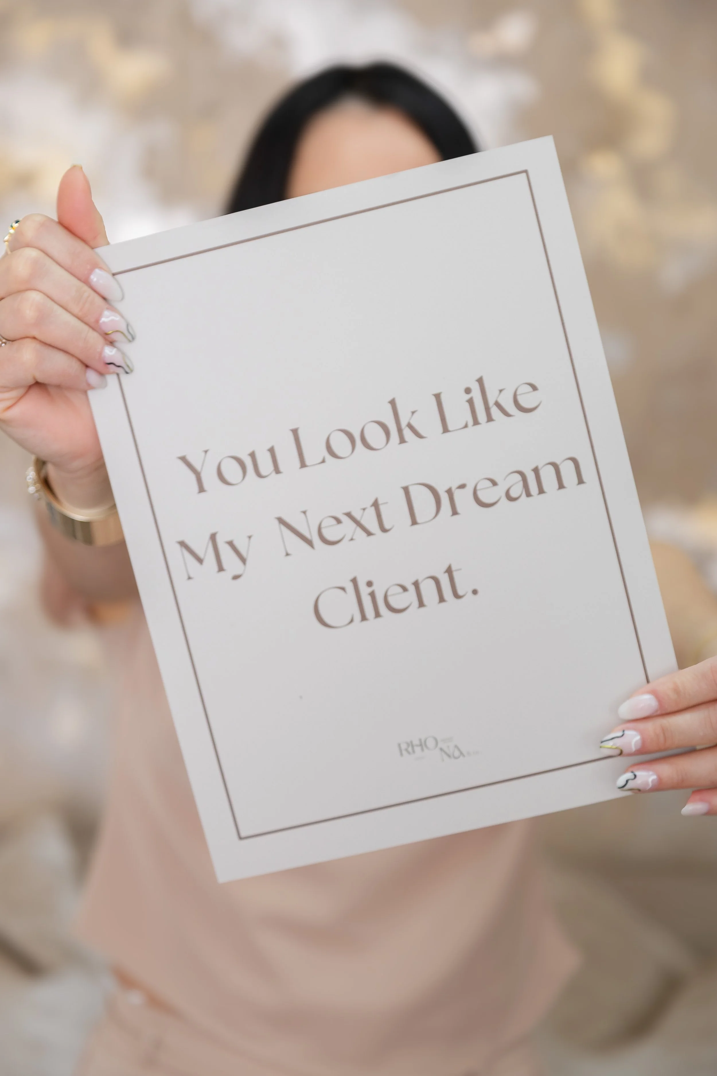 Person with manicured nails holding a sign that says, "You Look Like My Next Dream Client," partially obscuring their face.