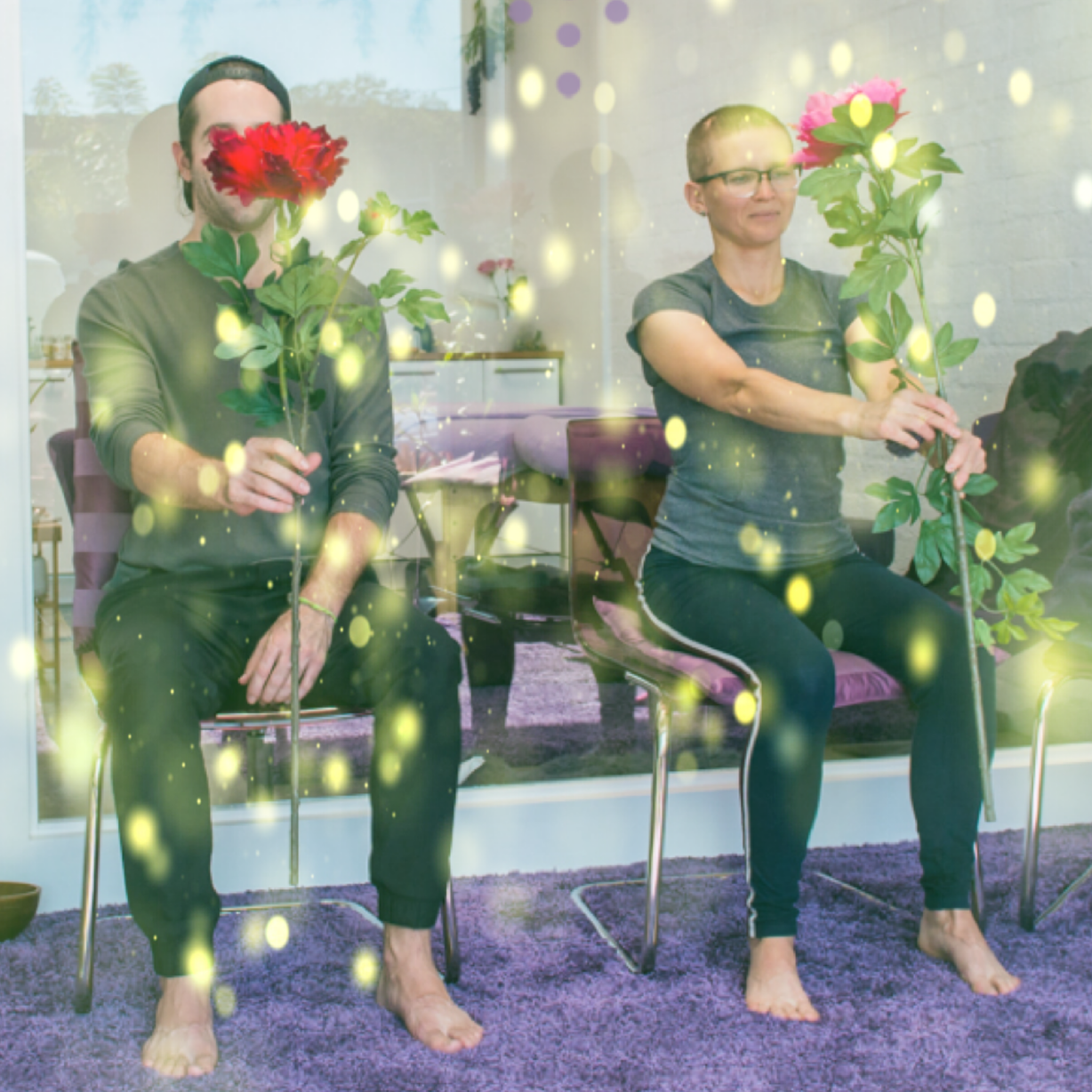 Two people sitting barefoot on chairs in a room, holding large colorful flowers, with a decorative overlay of yellow and purple light effects. Kismet is an intuitive living institute located in Venice, California, offering workshops, healing sessions