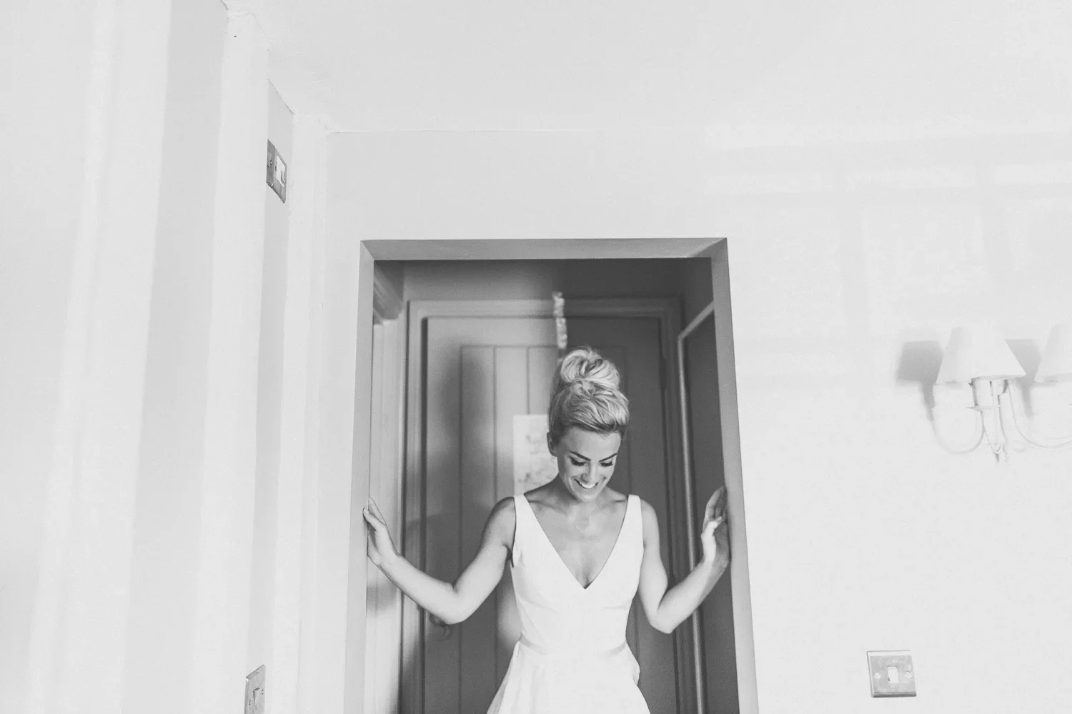 A woman in a white dress standing in a doorway, smiling, with her hands touching the doorframe on either side.
