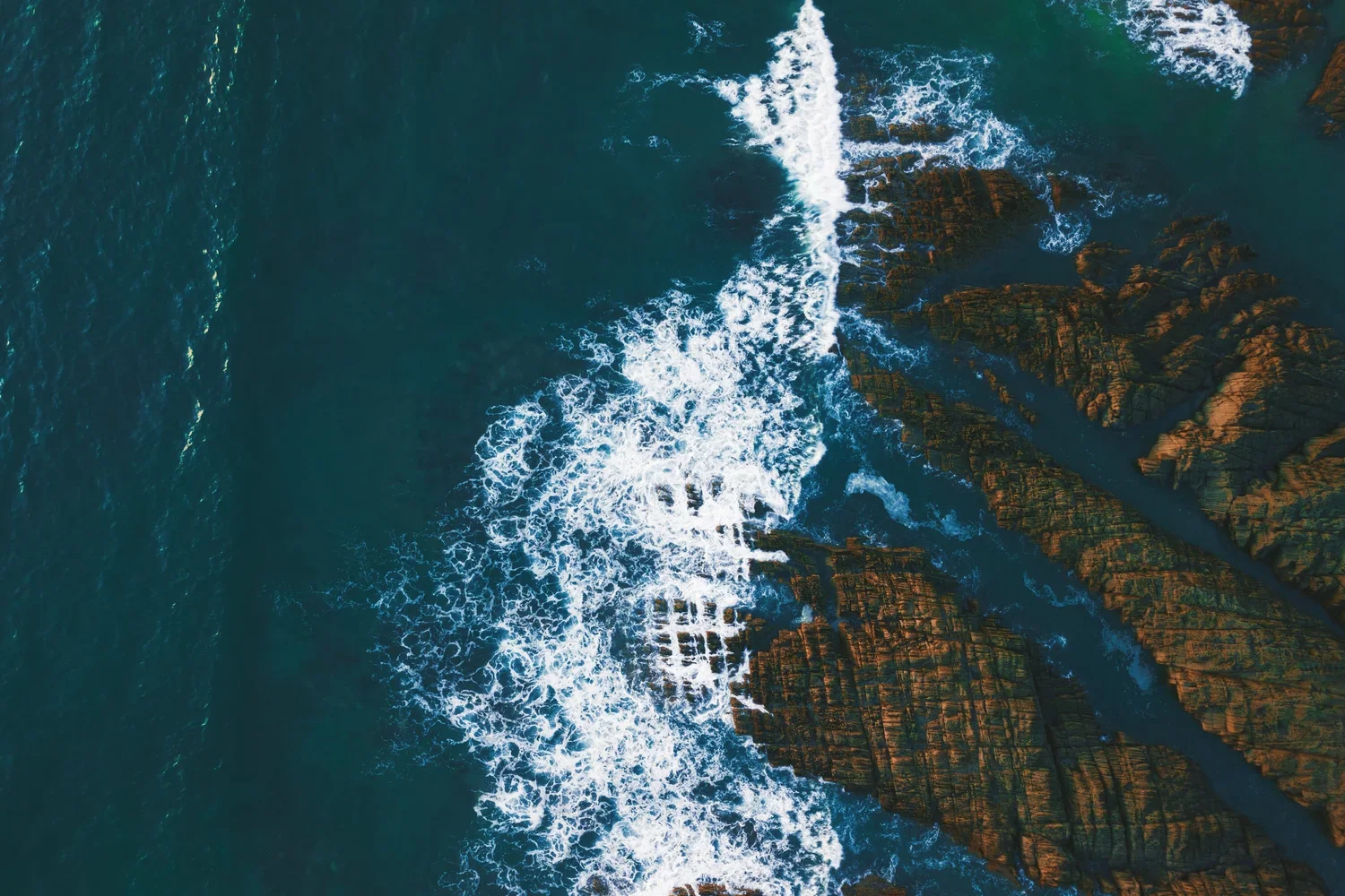 Aerial view of waves crashing against rocky shoreline and cliffs
