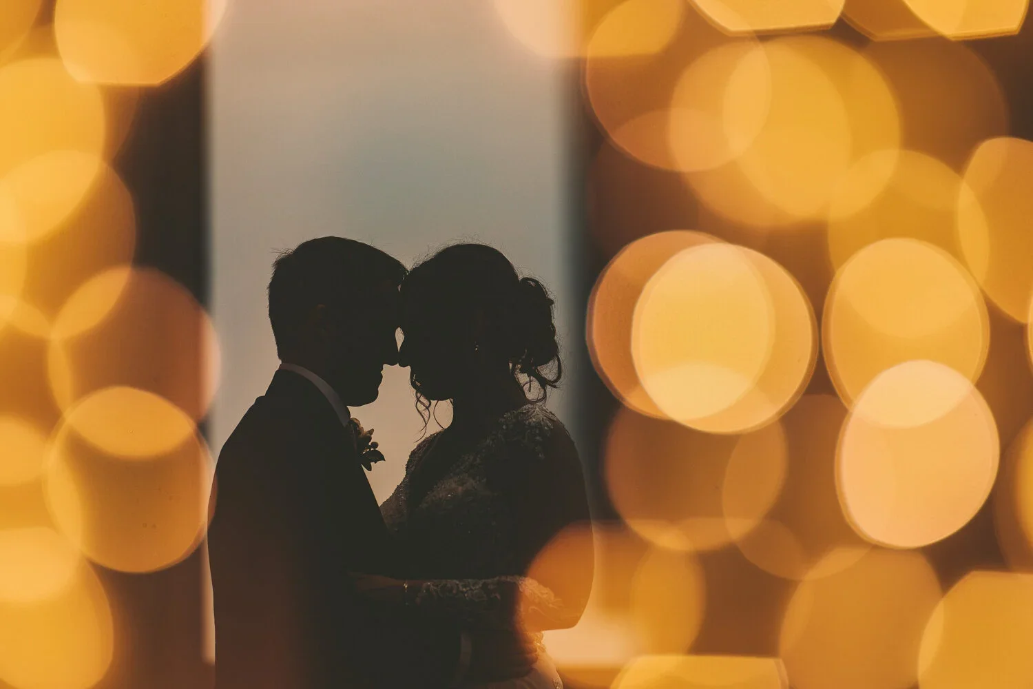 Silhouette of a couple dancing, with warm, glowing bokeh lights in the foreground, creating a romantic and intimate atmosphere.