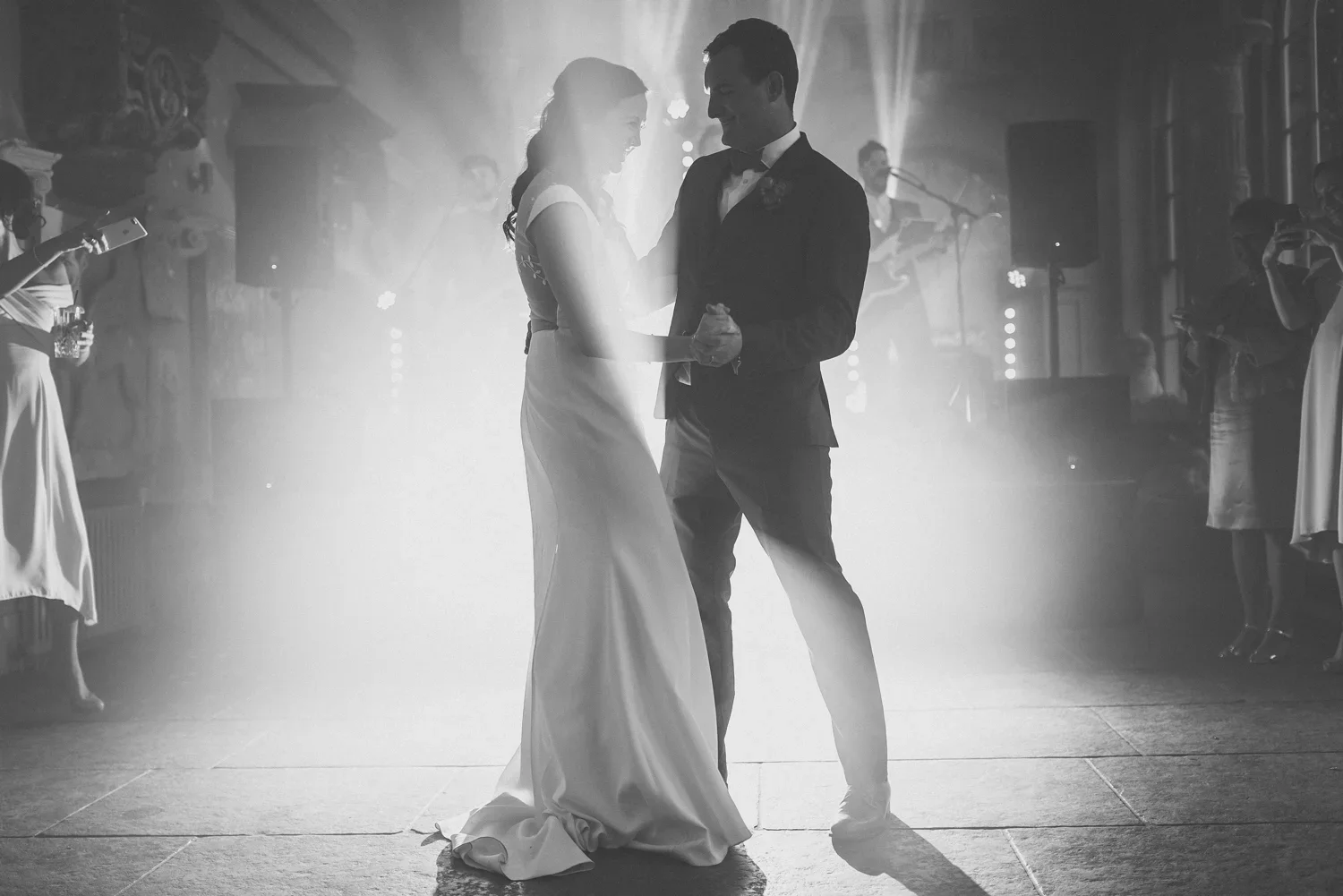 A bride and groom dancing during their wedding reception with a band playing in the background, black and white photo.