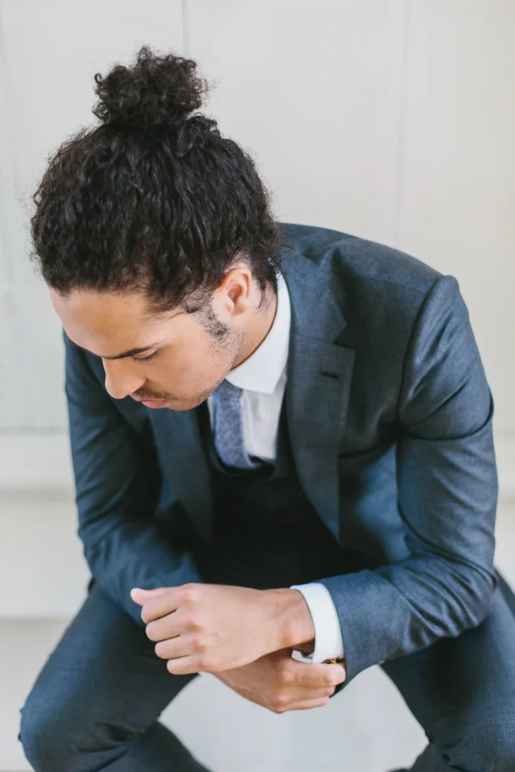 A young man in a business suit crouching down, holding his stomach with a pained expression, possibly indicating discomfort or illness.