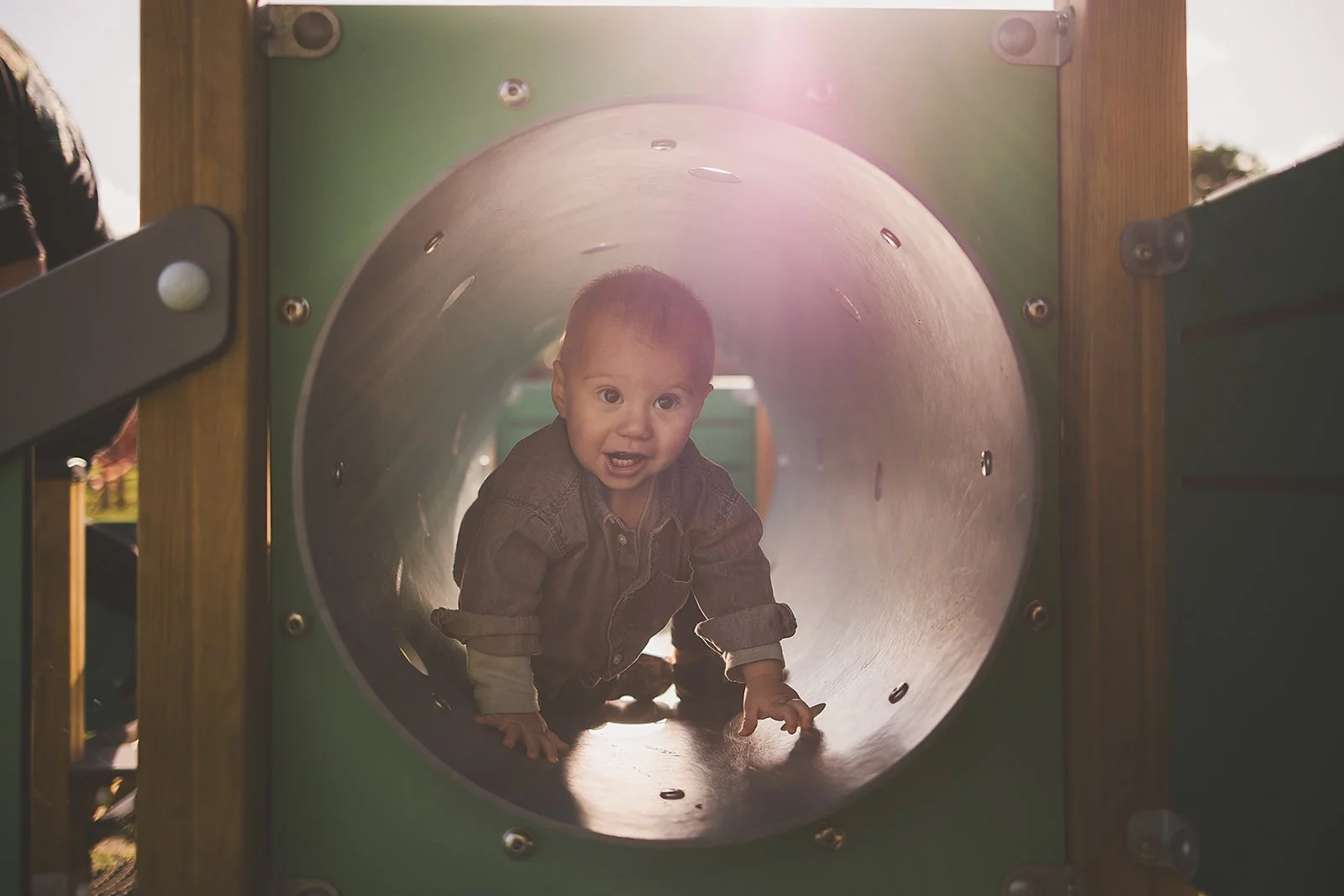 Child crawling through a playground tunnel with sunlight shining from behind.