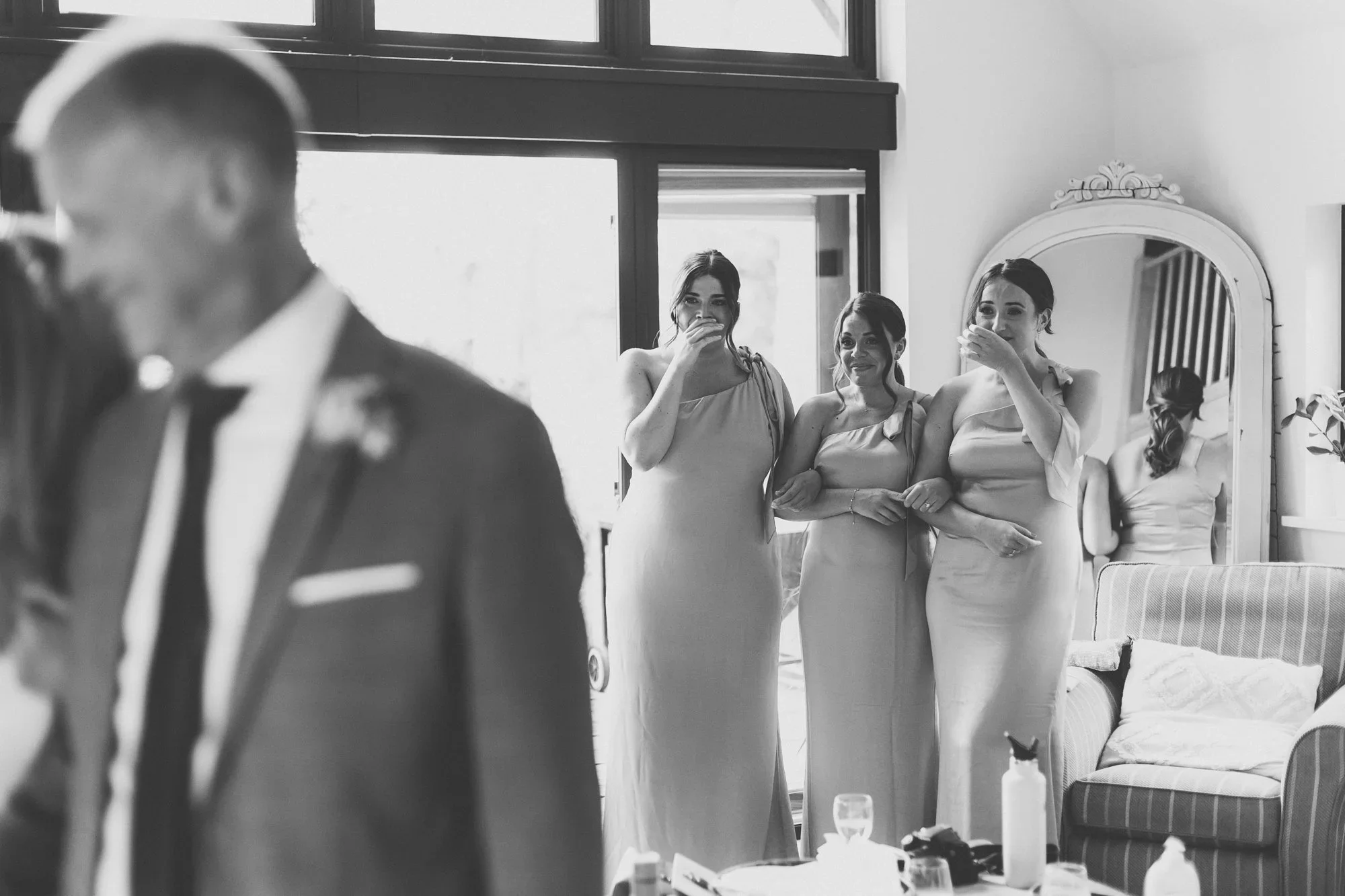 A black-and-white photo of three women in elegant dresses standing in a room, with two of them visibly emotional and crying, likely during a wedding or special event.