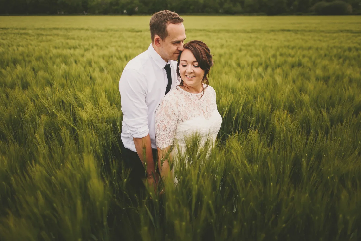 A couple standing close together in a green wheat field, smiling and enjoying each other's company.