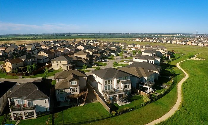 Aerial view of a suburban neighborhood with houses, lawns, and a walking trail on the right side during daytime.