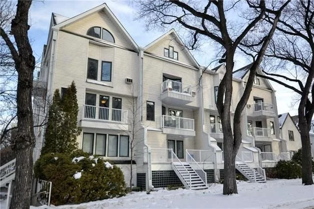 A multi-story residential building with beige siding and white balconies, set against a snowy landscape with leafless trees.