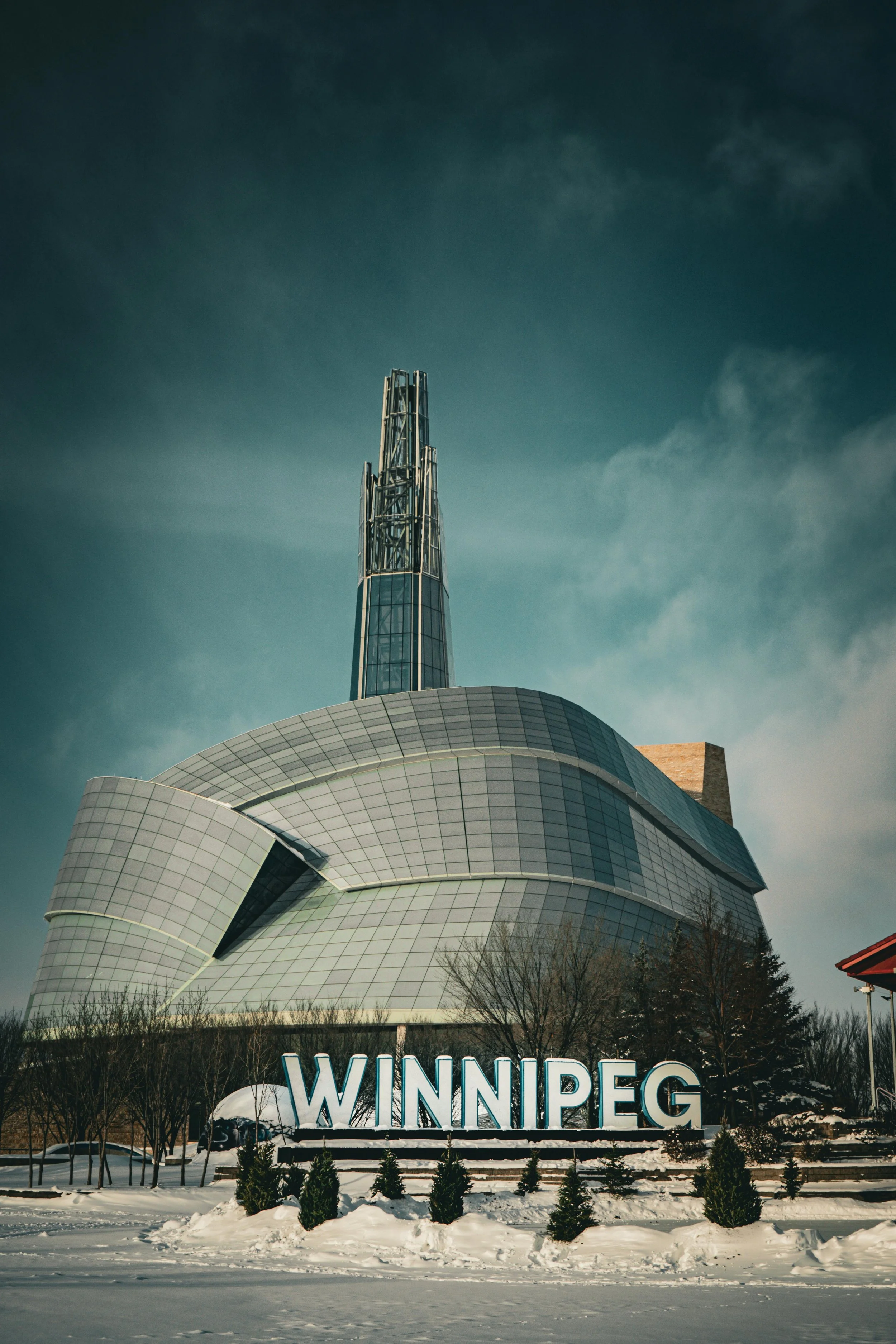 Salisbury in Winnipeg, Manitoba, with a modern building featuring a tall spire and large sign that reads 'WINNIPEG', surrounded by snow and small bushes.