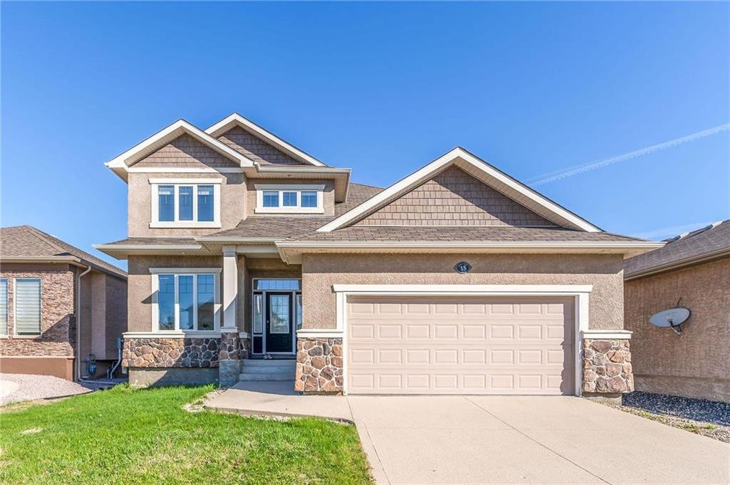 Front view of a two-story house with beige siding and stone accents, a two-car garage, and a small front lawn, under a clear blue sky.