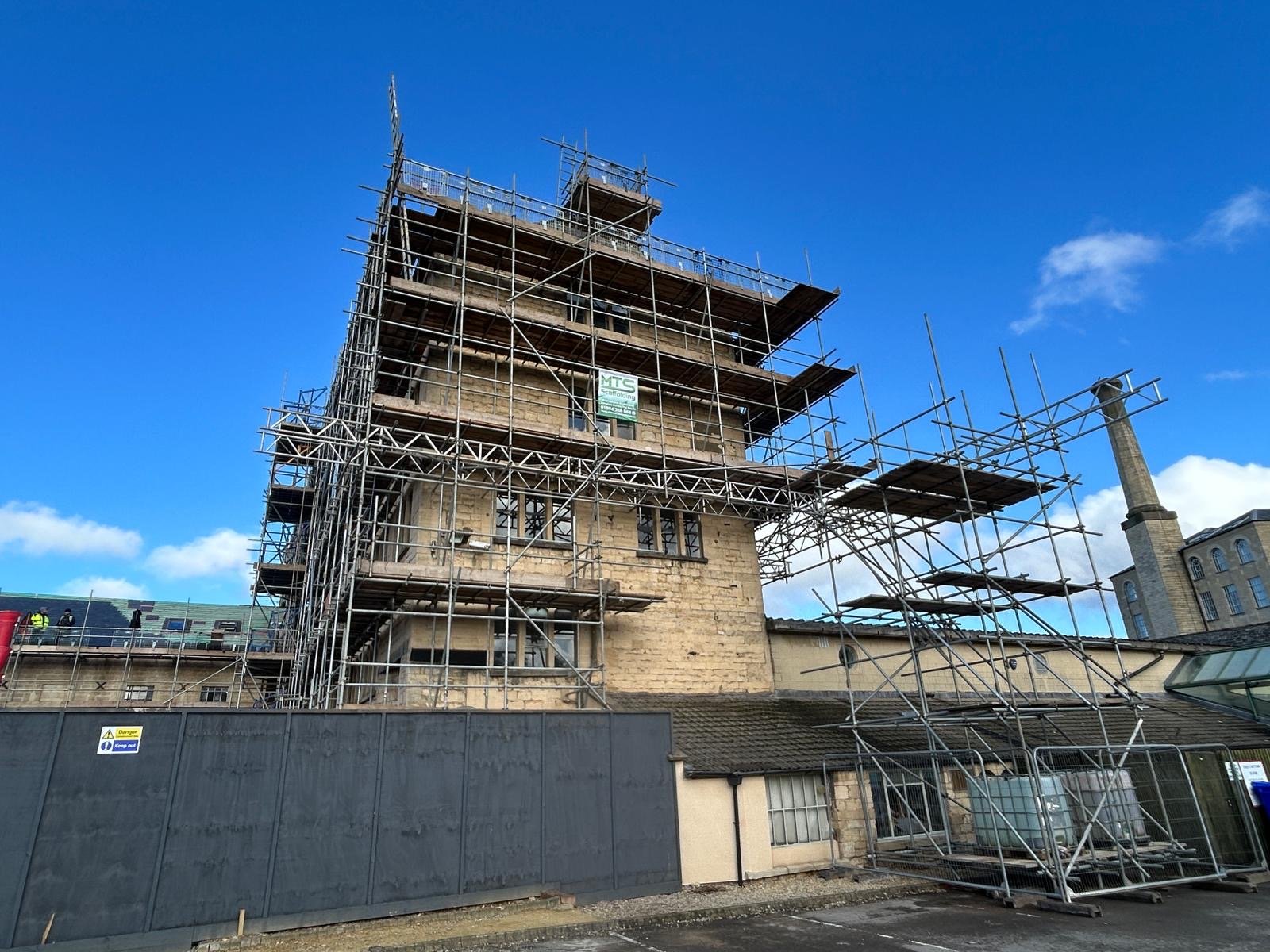 Building under renovation with scaffolding around it, set against a blue sky with some clouds.