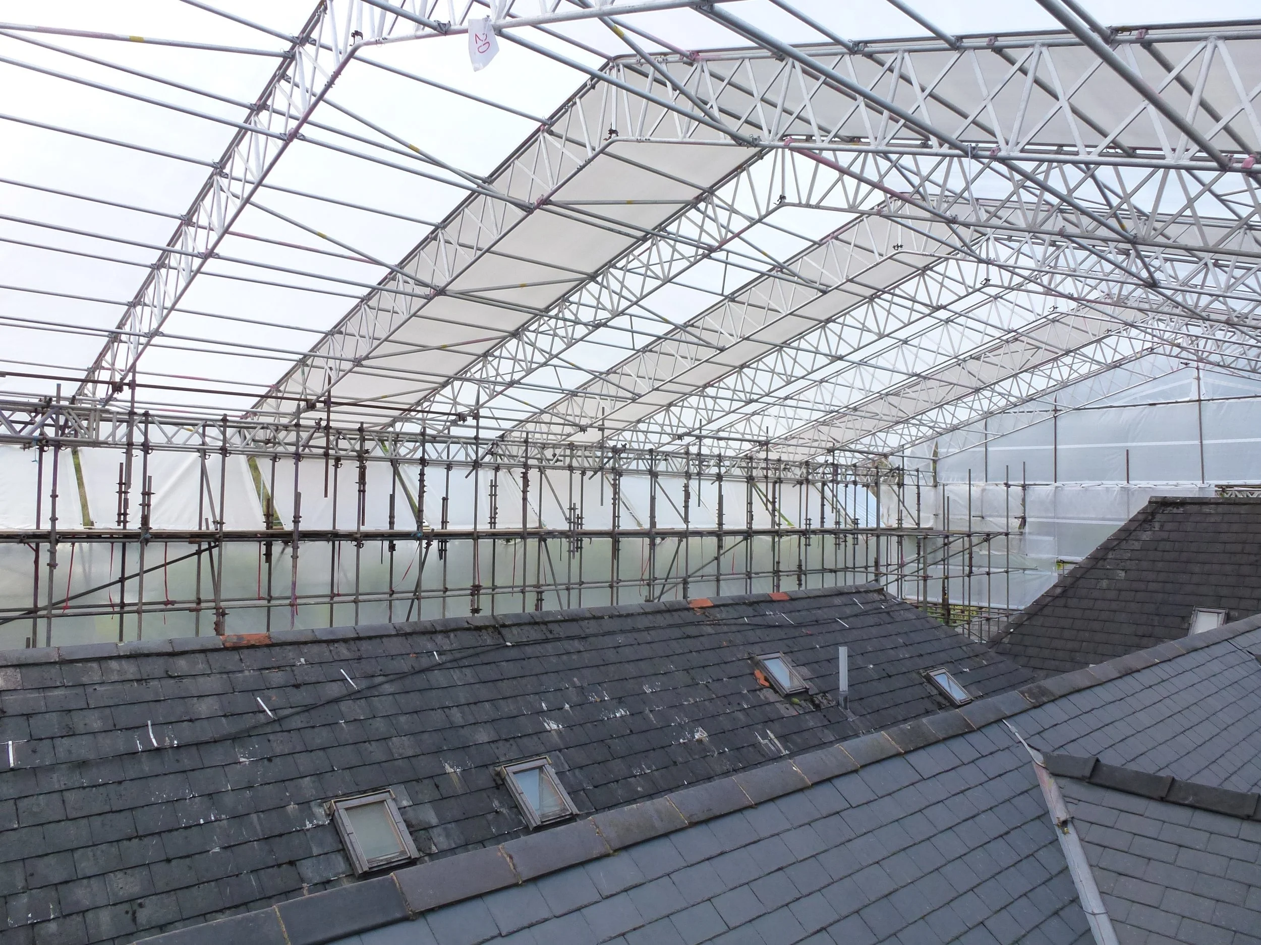 Scaffolding structure set up above residential rooftops with skylights, and a large, open framework, possibly for construction or renovation work.