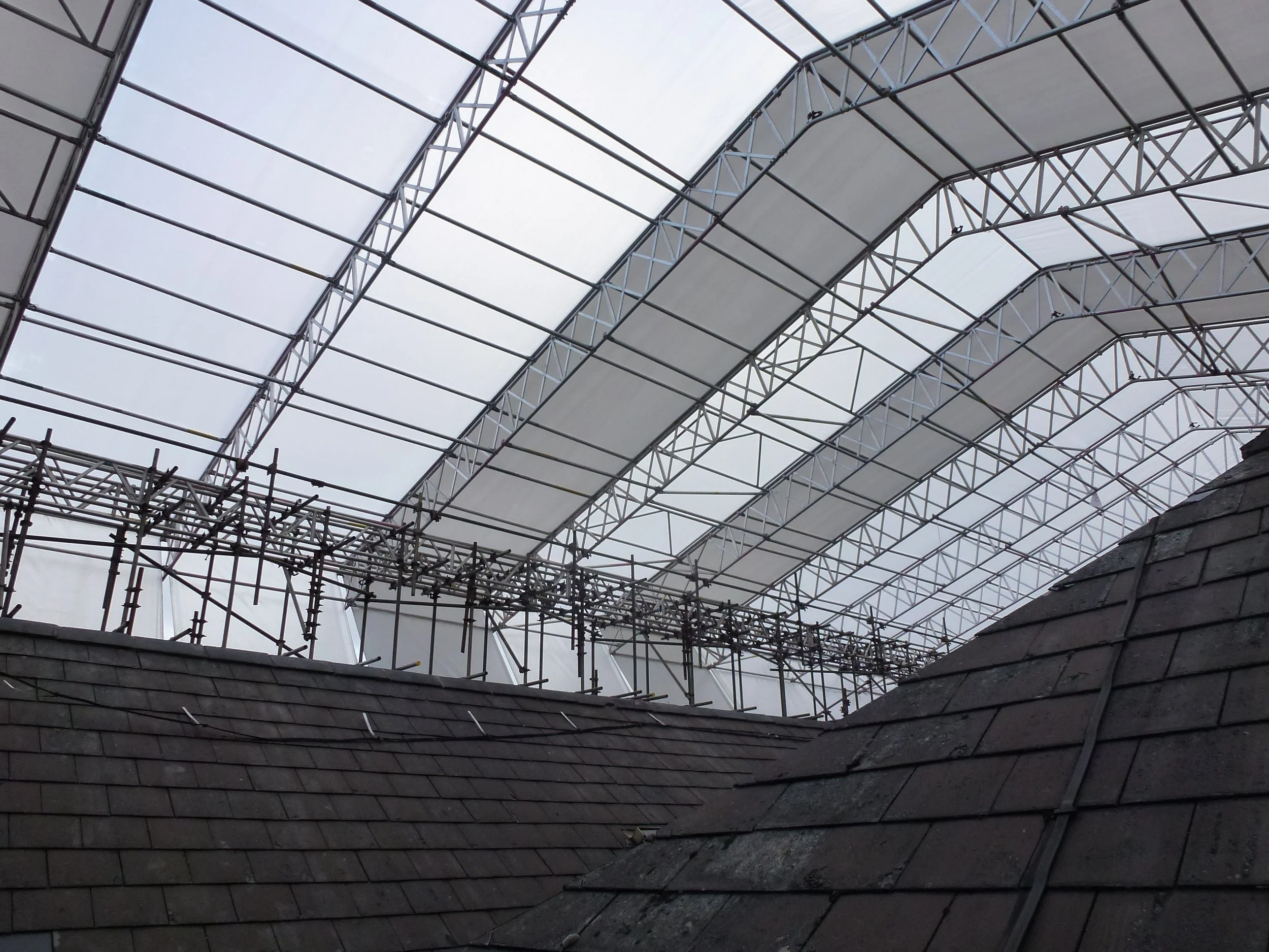 Construction scaffolding and a partially covered roof underneath a large arched construction area with a translucent roof.