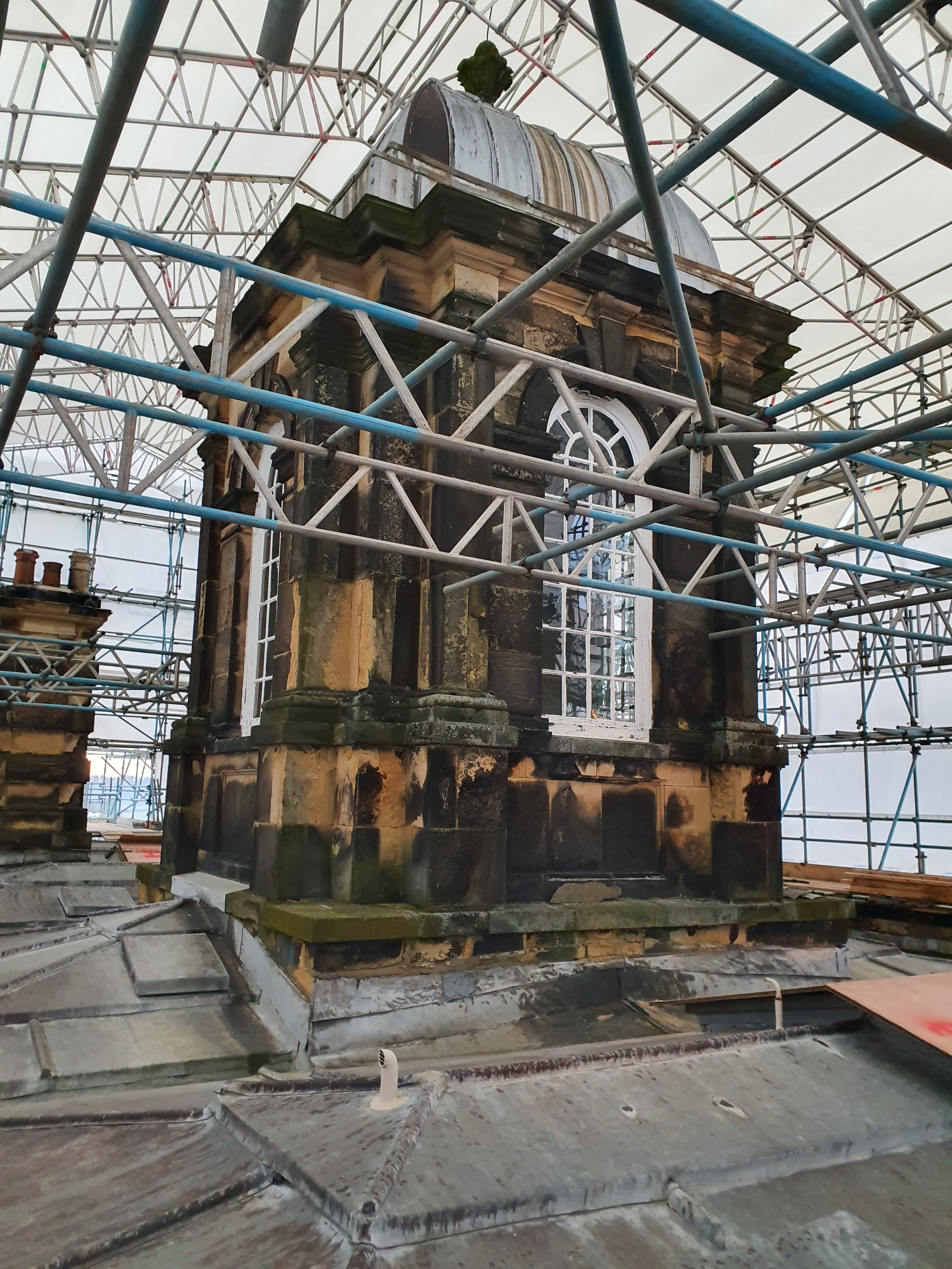 A close-up of a historic stone building with a decorative roof, surrounded by metal scaffolding during renovation.