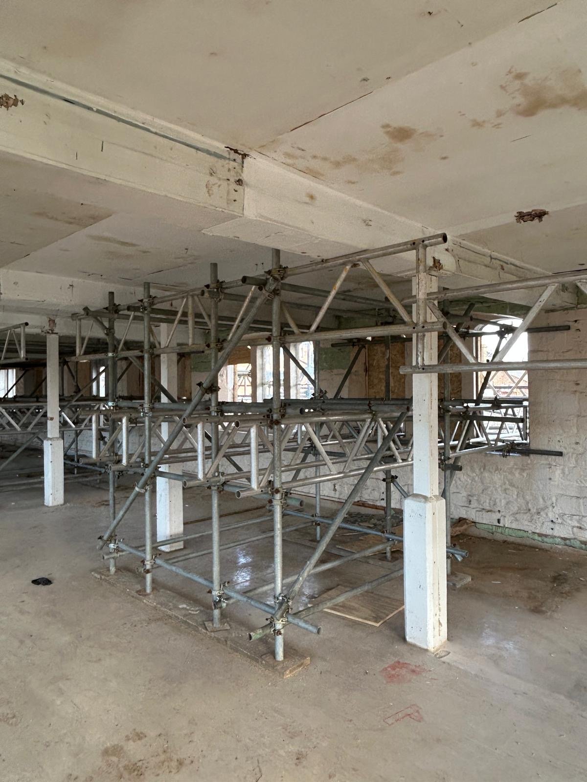Indoor construction site with metal scaffolding and unfinished walls and ceiling.