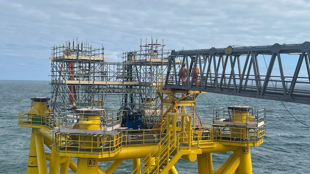 Offshore oil rig with yellow structure and scaffolding, set on the ocean under a cloudy sky.