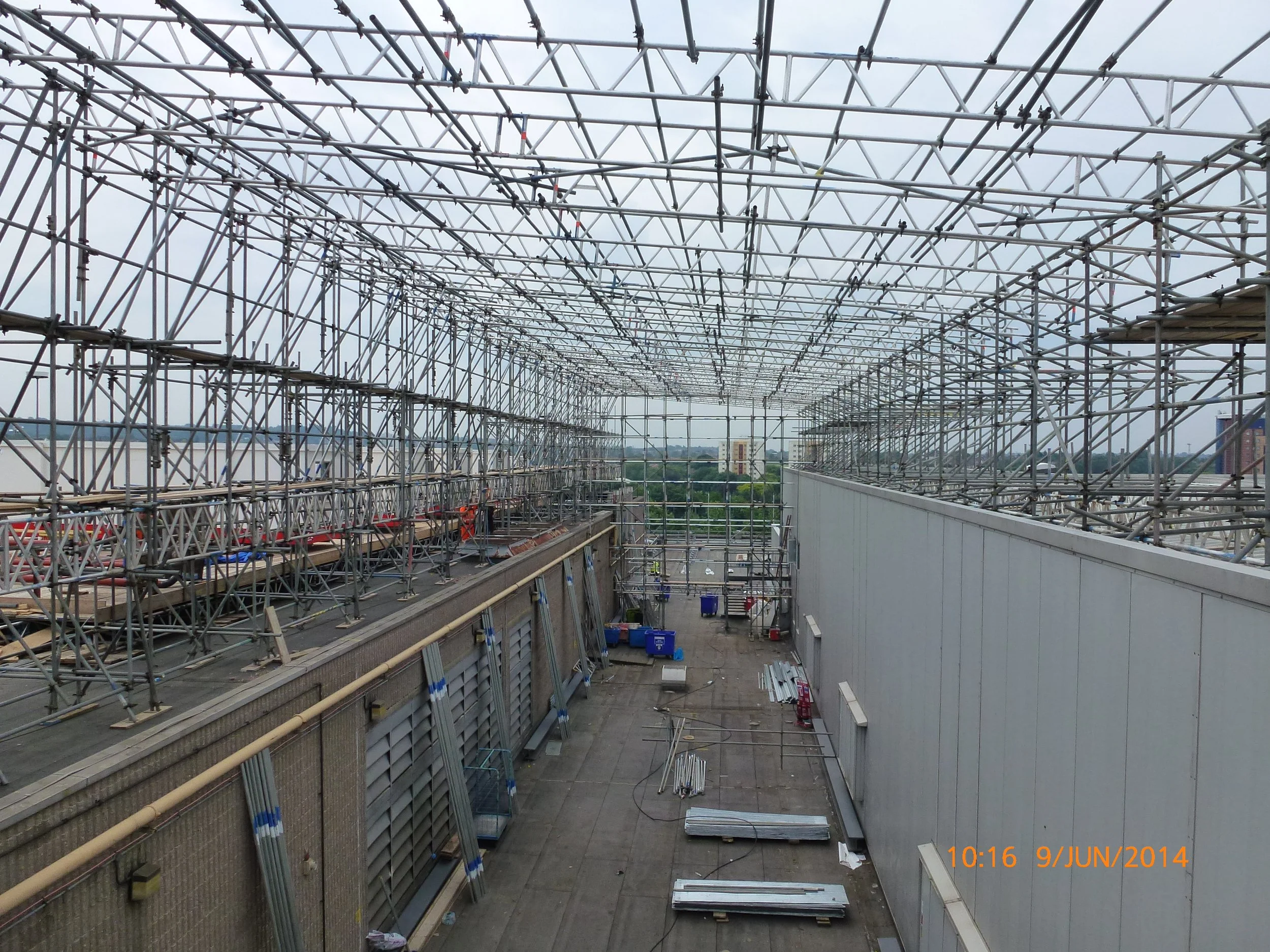 Construction site with extensive metal scaffolding on top of a building under renovation, showing a cloudy sky in the background. Date and time stamp: 10:16, June 9, 2014.