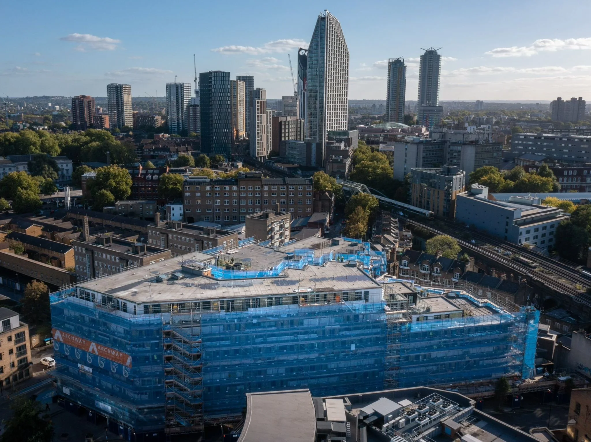 Aerial view of a city skyline with tall modern buildings and a construction site covered in blue scaffolding.
