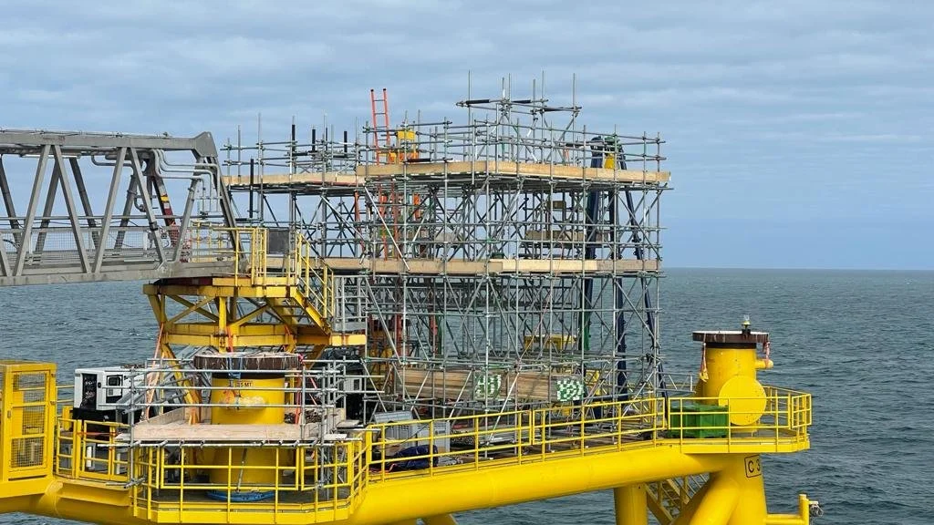 Offshore oil or gas platform with scaffolding and safety railings, located in the ocean under cloudy sky.
