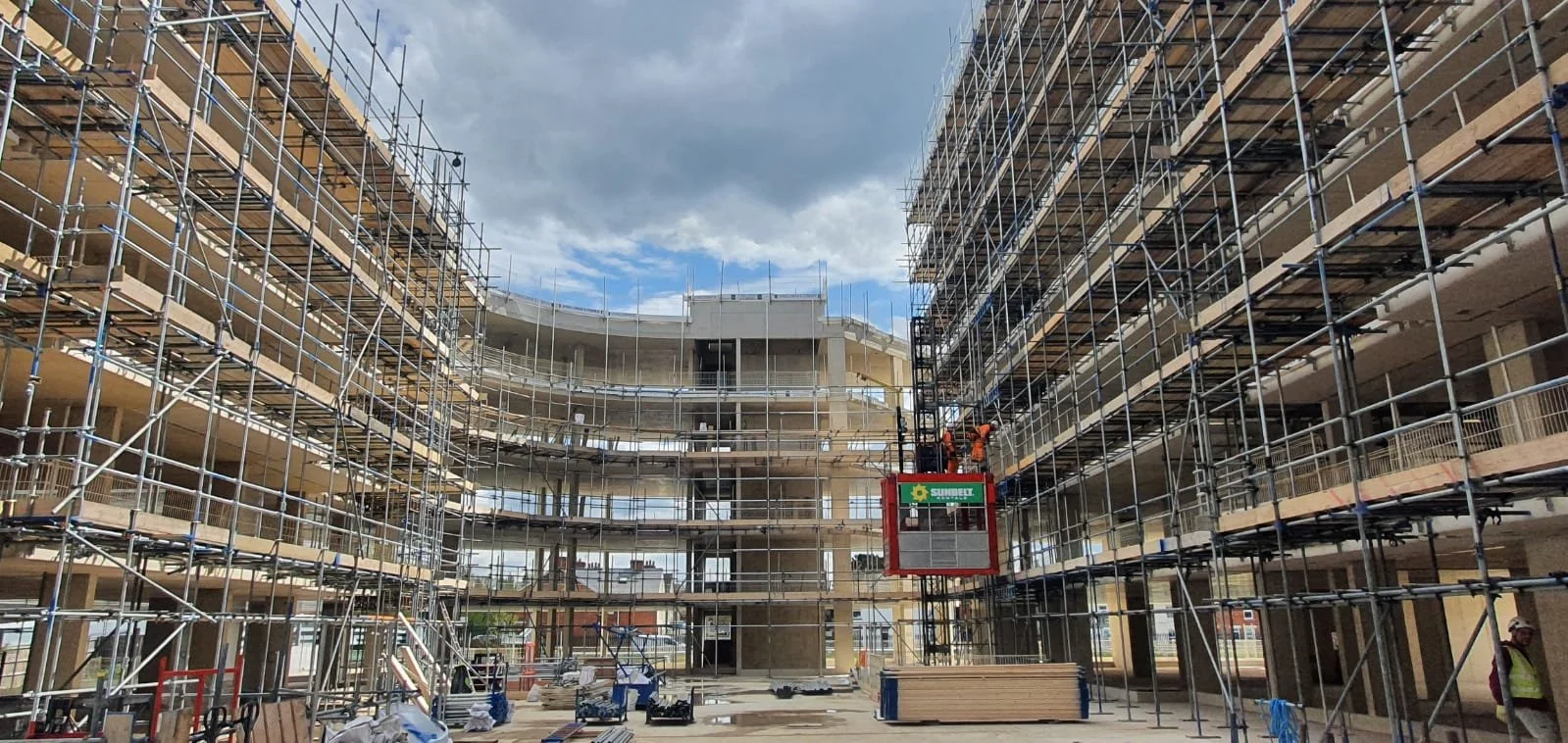 Construction site with scaffolding around a multi-story building under construction, with workers and construction equipment present.