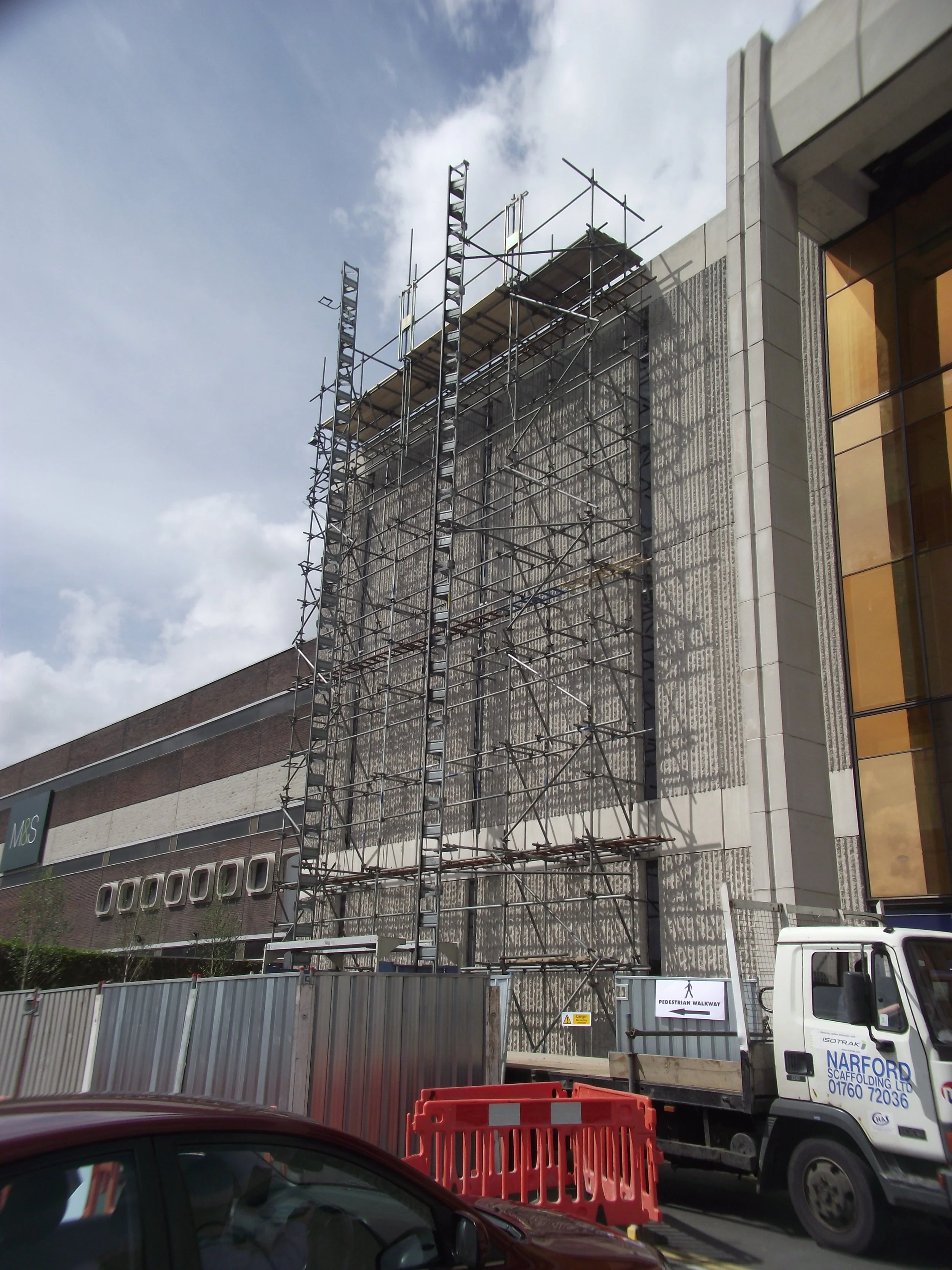 Building under construction with scaffolding, safety barriers, and construction signage.