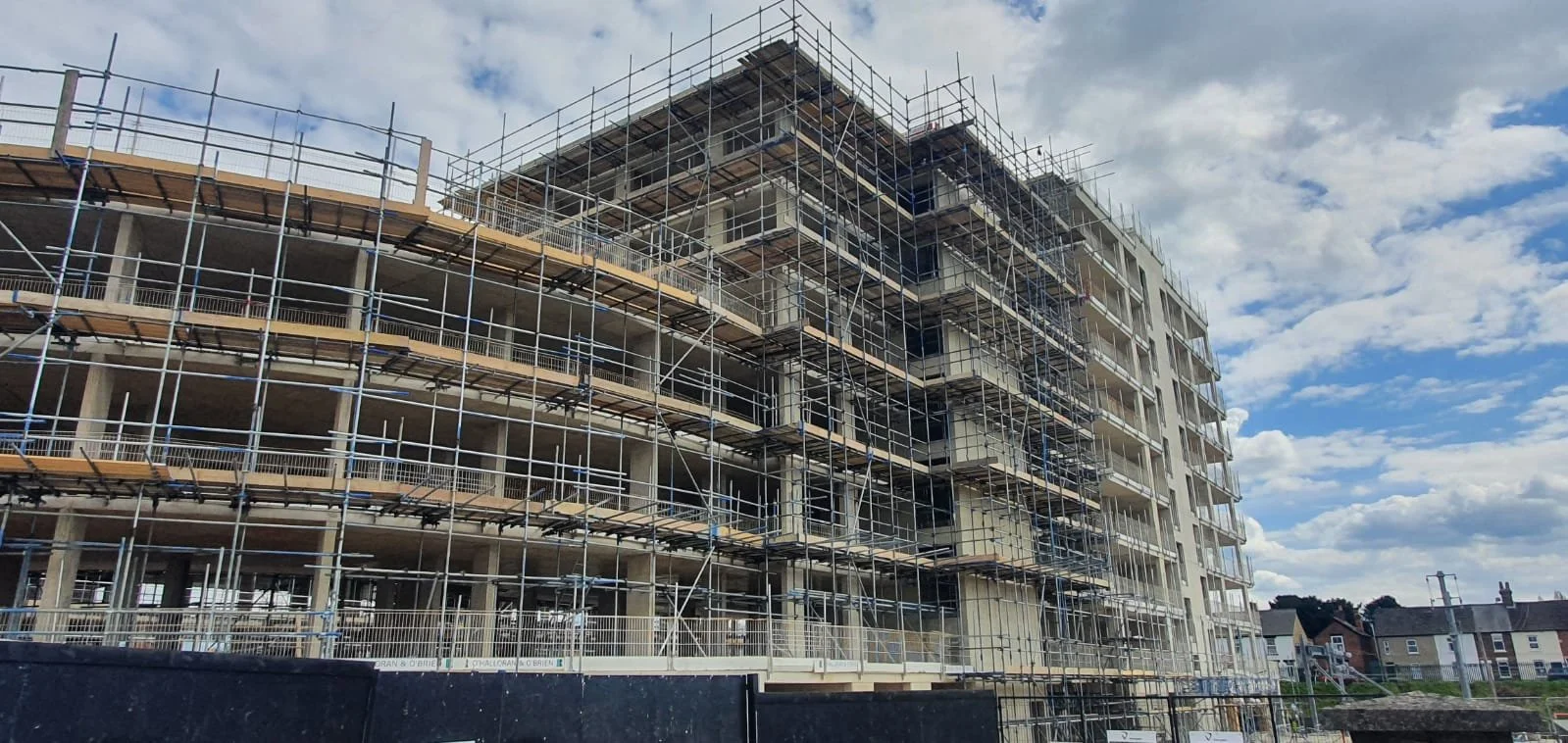 Construction site with a multi-story building surrounded by scaffolding under a partly cloudy sky.