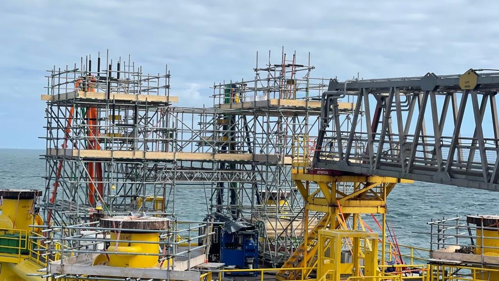 Construction site on a pier over water with scaffolding and a yellow crane.