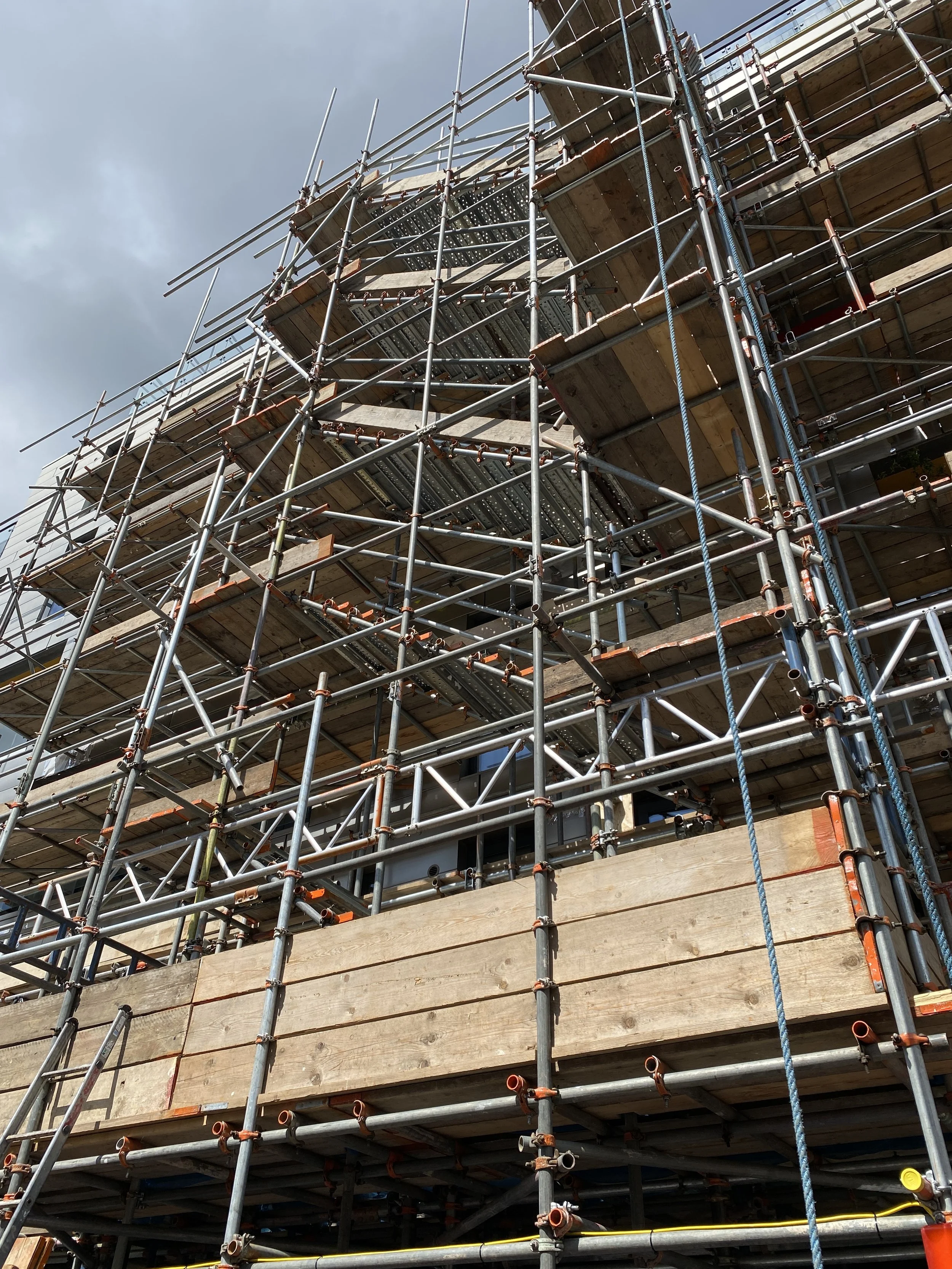 Construction scaffolding surrounding a building under construction, with wooden planks and metal poles visible.