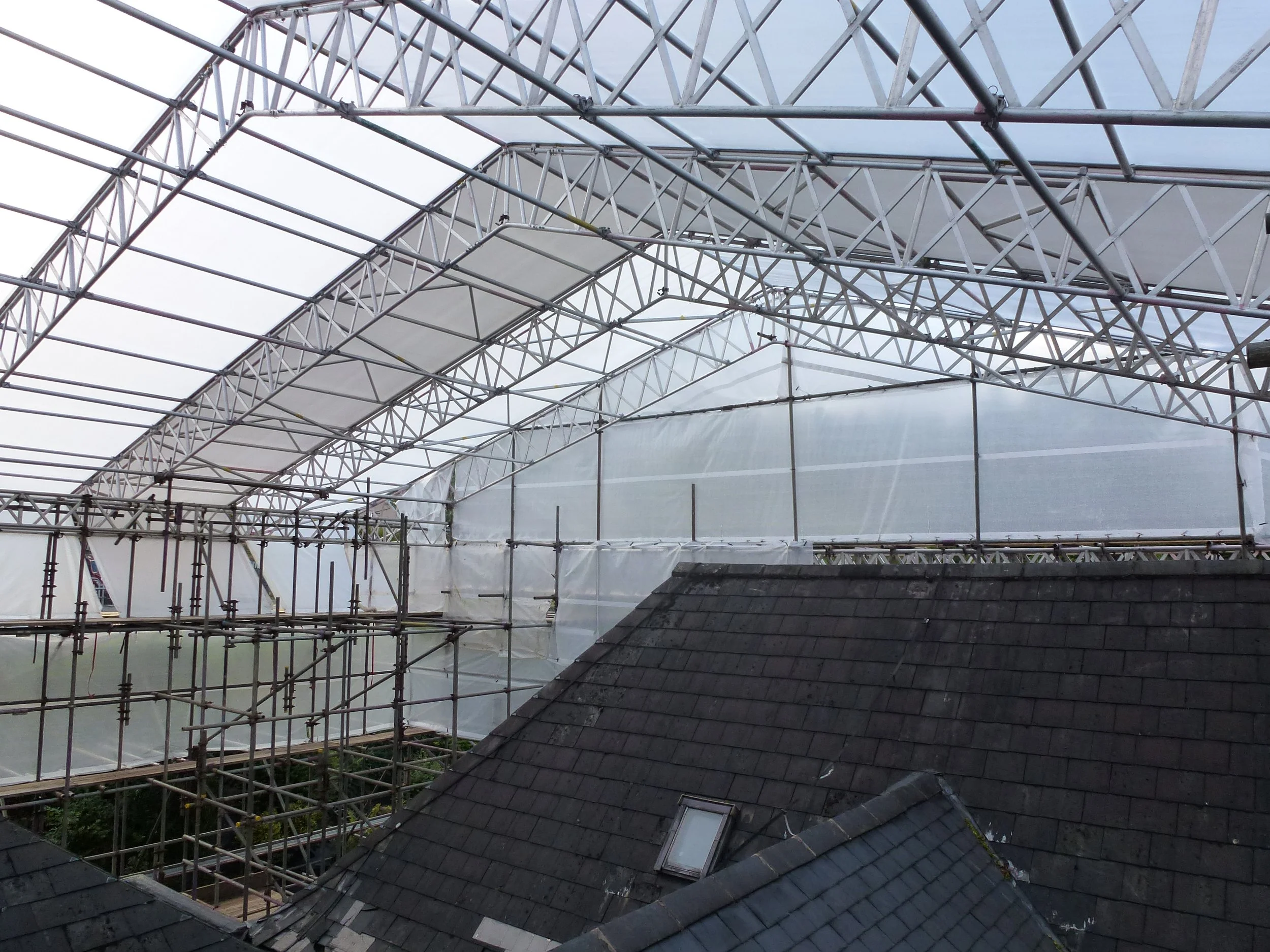 Scaffolding and construction framework on a roof, with plastic sheeting covering parts of the structure.