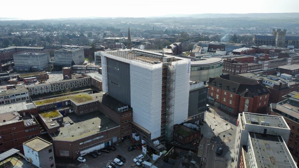 An aerial view of a cityscape with a large modern building under construction, surrounded by other commercial and historic buildings with scaffolding round it