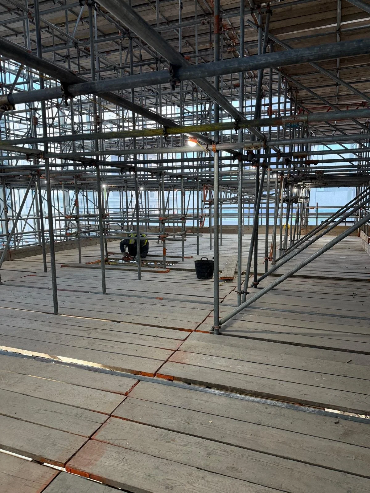 Scaffolding and construction materials inside a building under construction, with a worker working near the center.