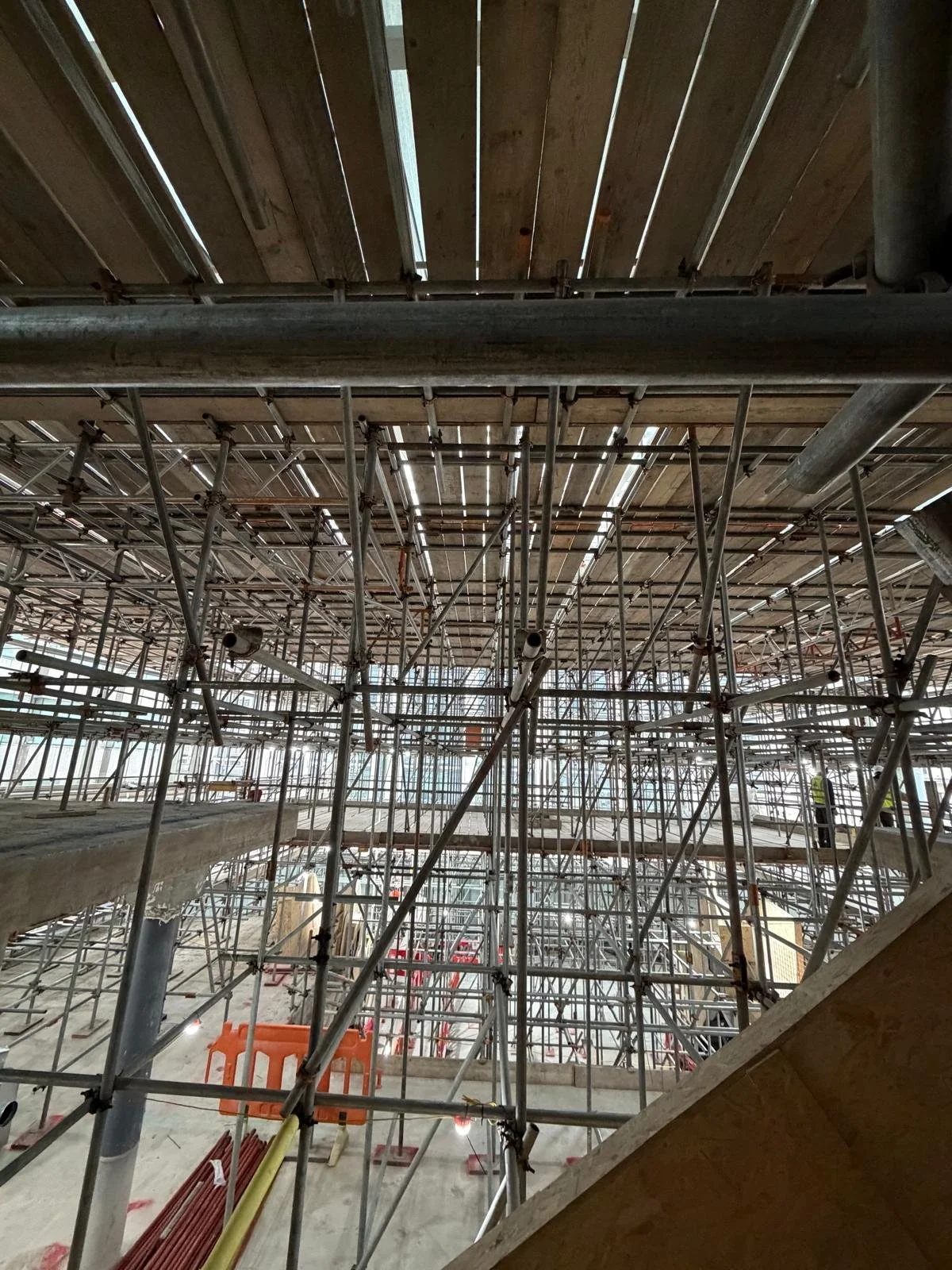 Inside a building under construction with metal scaffolding and a wooden ceiling.
