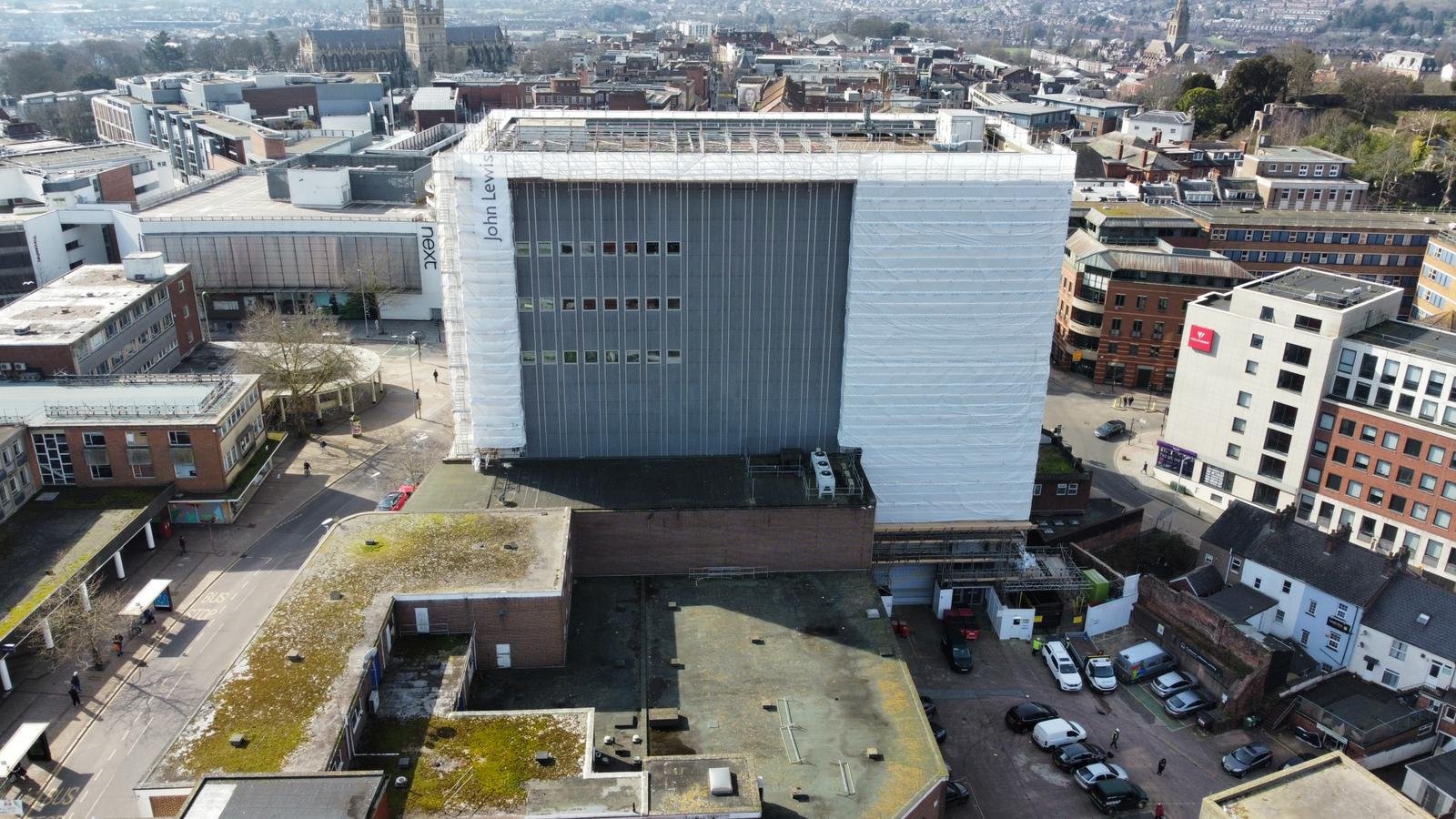 Aerial view of a cityscape with various modern buildings, streets, parking lots and some visible greenery.