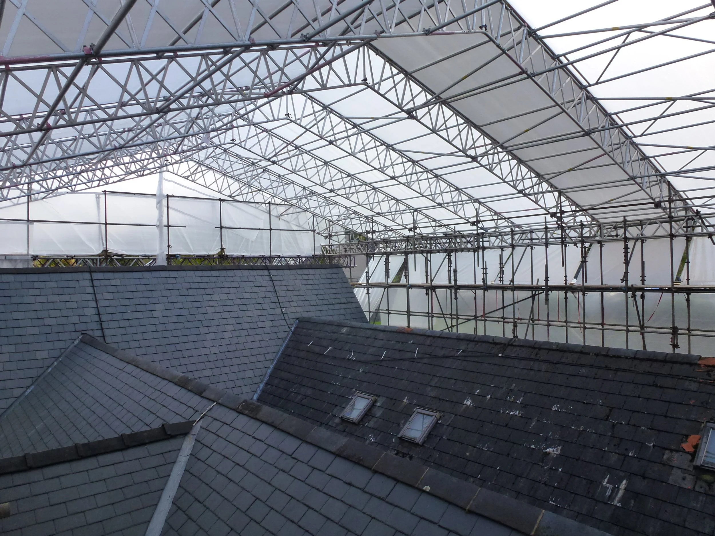 View of a roof under construction with scaffolding and a protective covering overhead.