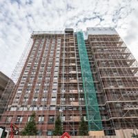 View of a tall building under construction with scaffolding and safety netting, in an urban setting.