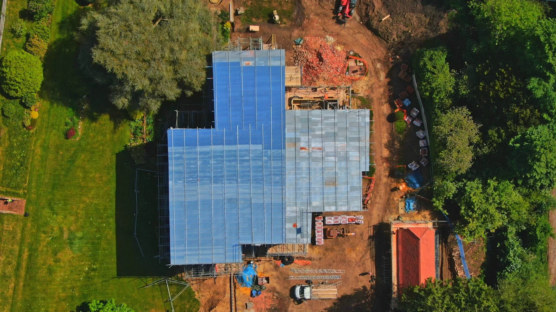 Aerial view of a house under construction with a new roof, surrounded by greenery and trees.