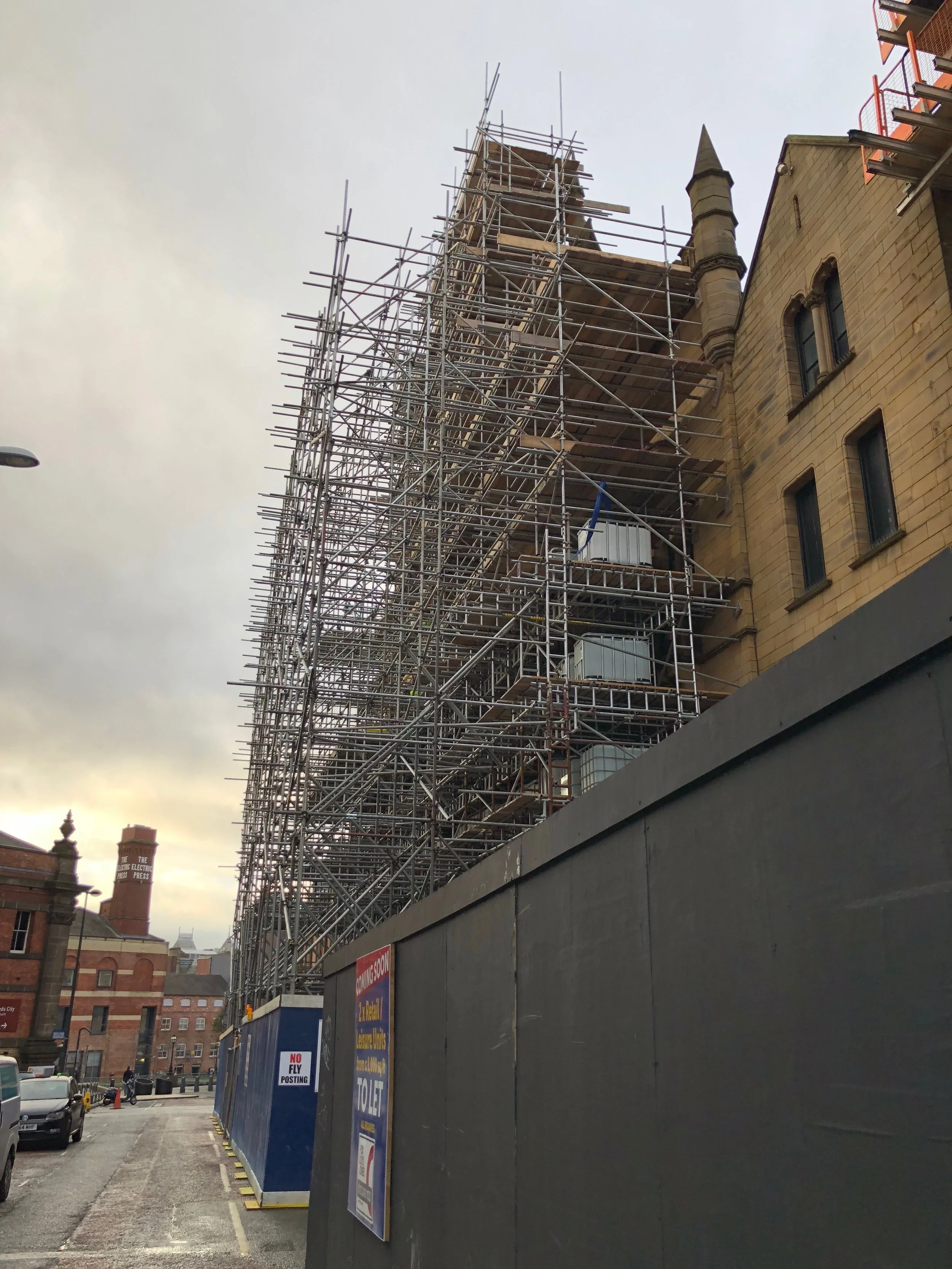 Scaffolding around a historic building under maintenance or renovation, with a cloudy sky in the background.