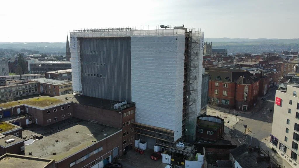 A large building under construction wrapped in white scaffolding in an urban area.