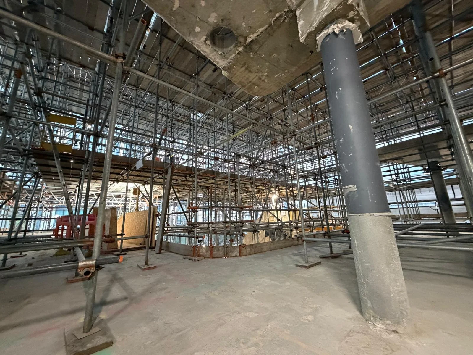 Construction site with scaffolding, metal pipes, concrete pillars, and unfinished concrete floor.