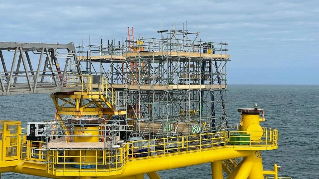 Offshore oil platform with scaffolding and yellow safety railings, located in the ocean under a cloudy sky.
