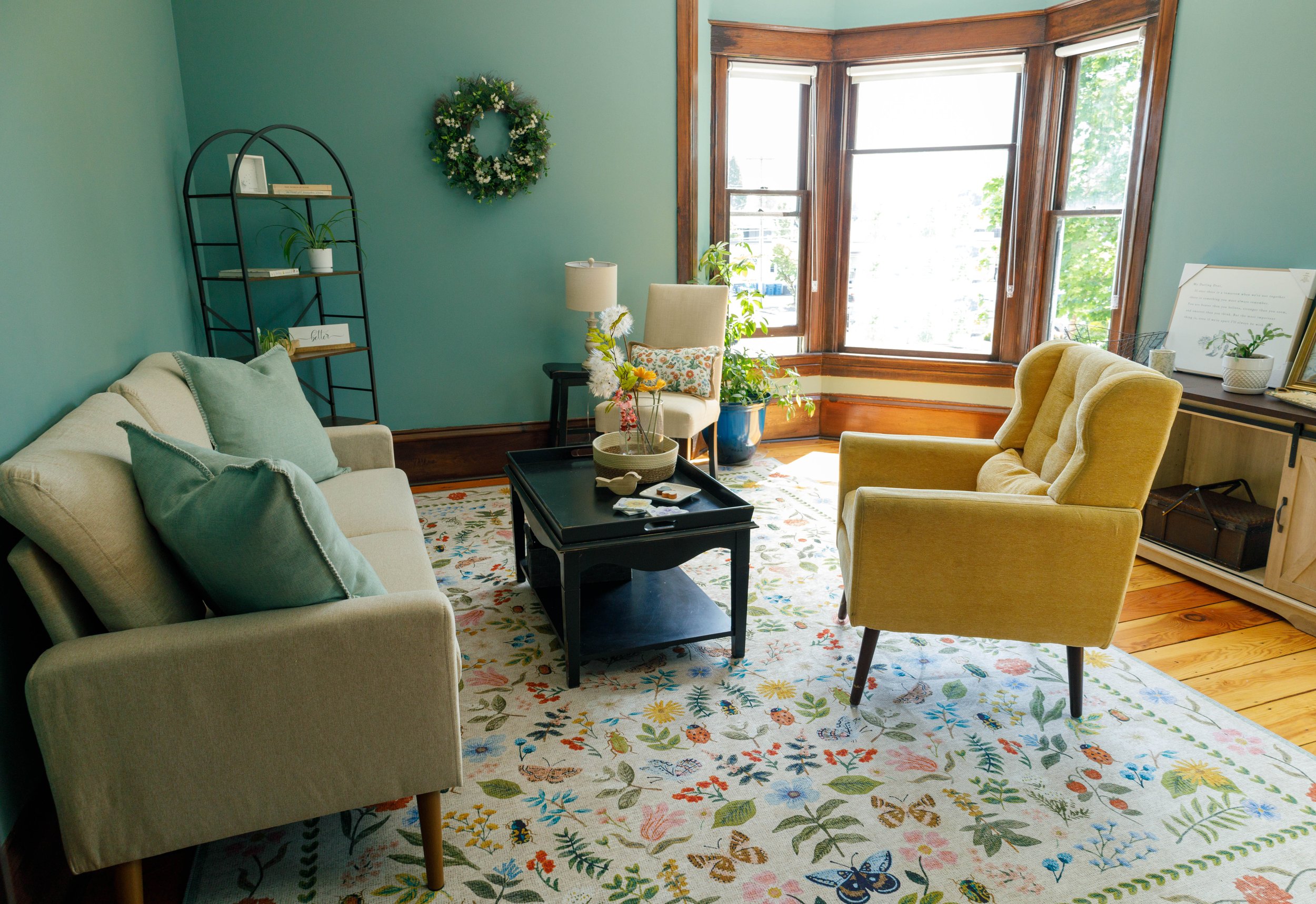 A cozy corner of a living room with two matching yellow armchairs, a small wooden side table with a lamp, a plant, and wooden floors near large windows with dark wood trim.