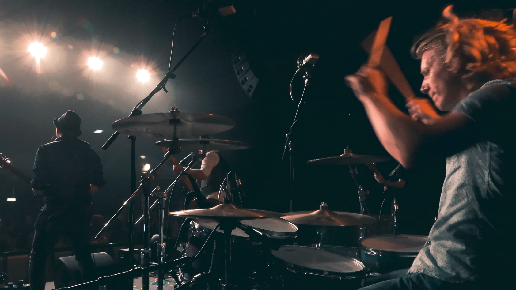 Musicians performing on stage with drums and microphones under bright stage lights