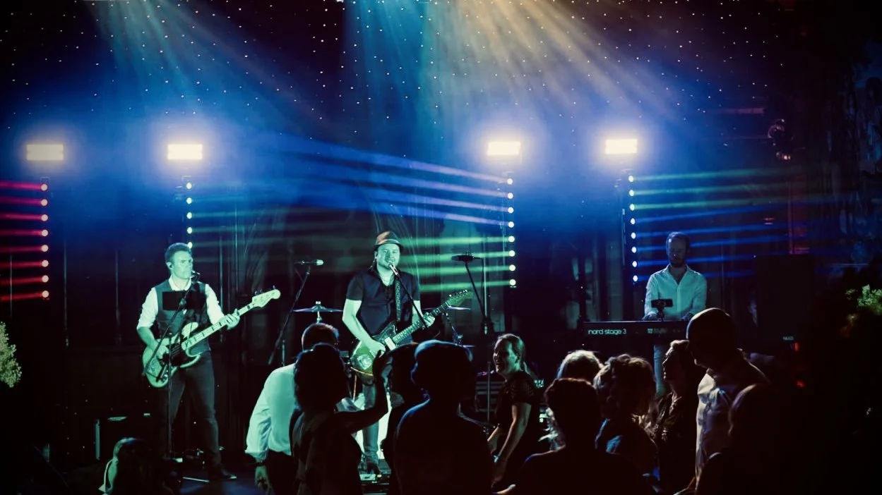 Band performing live on stage with colorful lights and audience dancing.