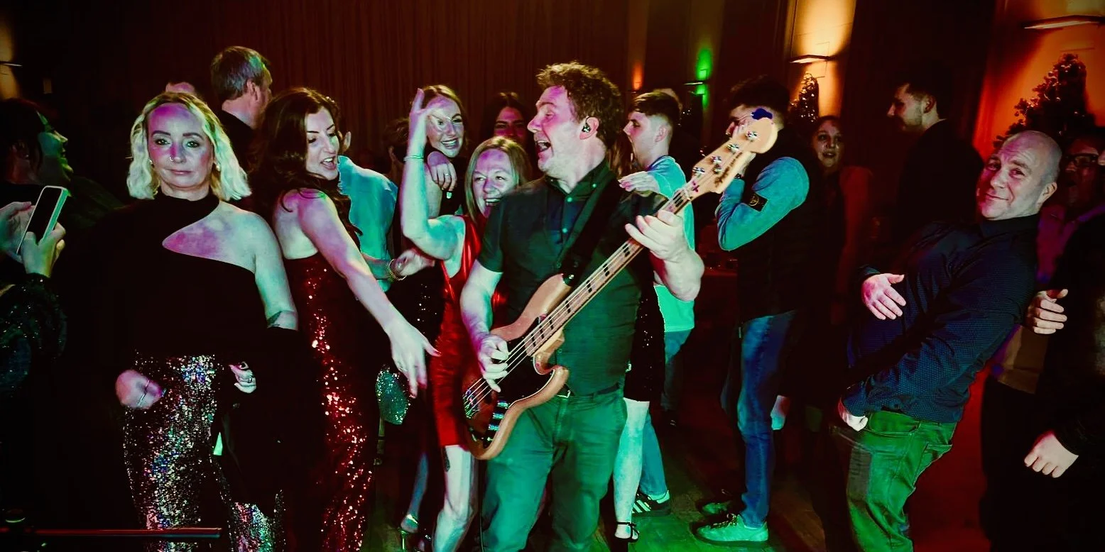 A group of people at a party dancing and enjoying music, with a man playing bass guitar.