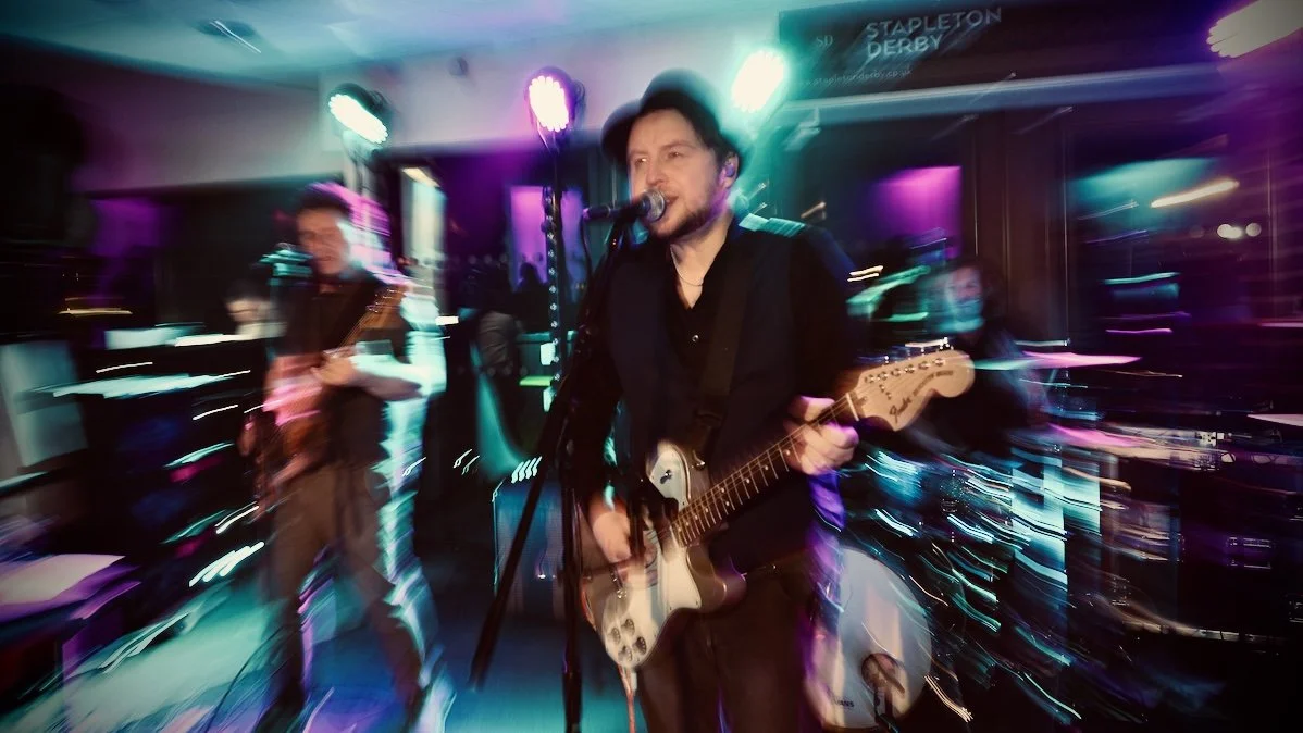 Band performing on stage with colorful lights, focused on lead singer playing electric guitar and singing into microphone