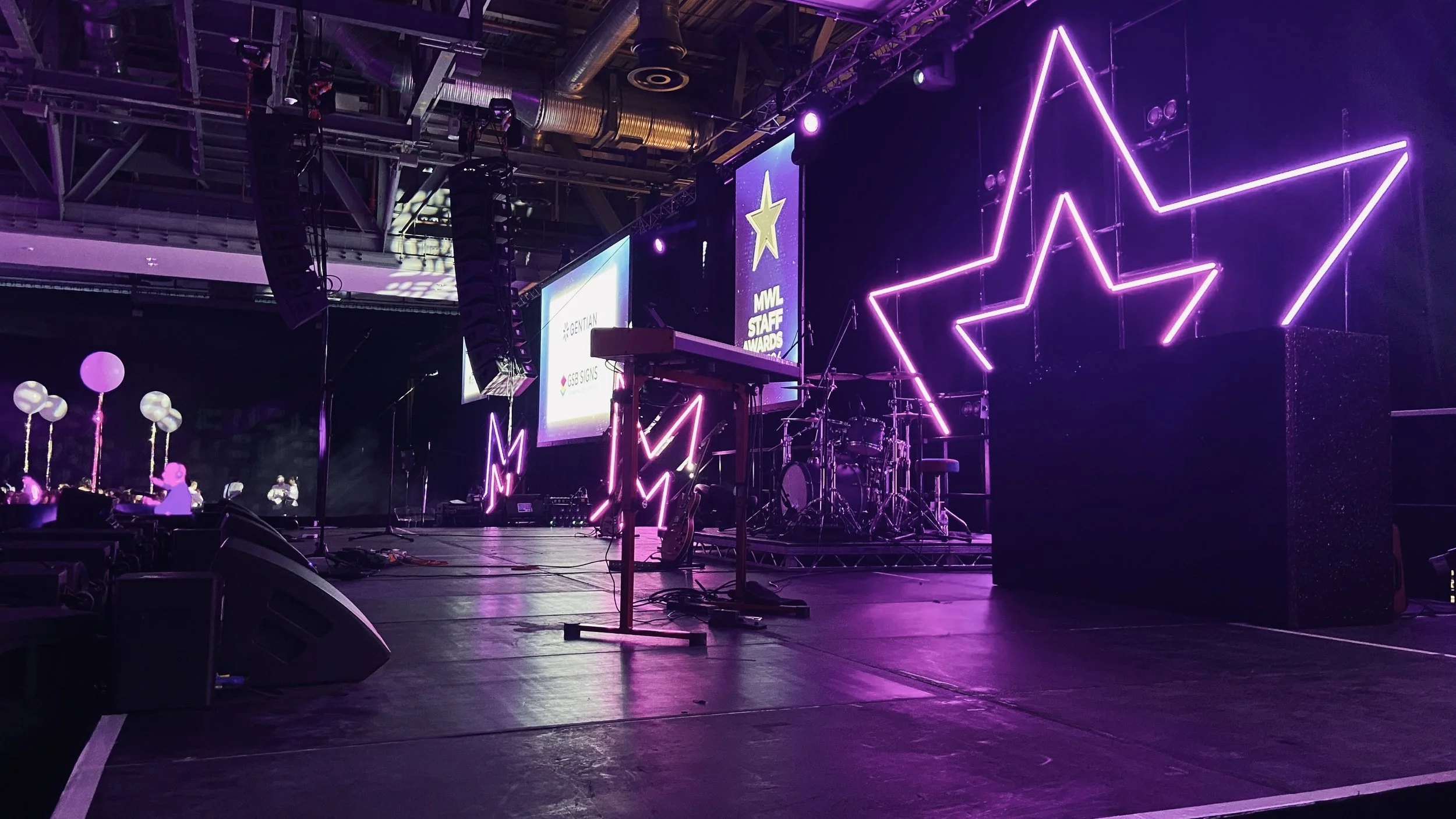 Stage setup with purple neon star decorations, musical instruments, and screens displaying awards, illuminated for an event or concert.