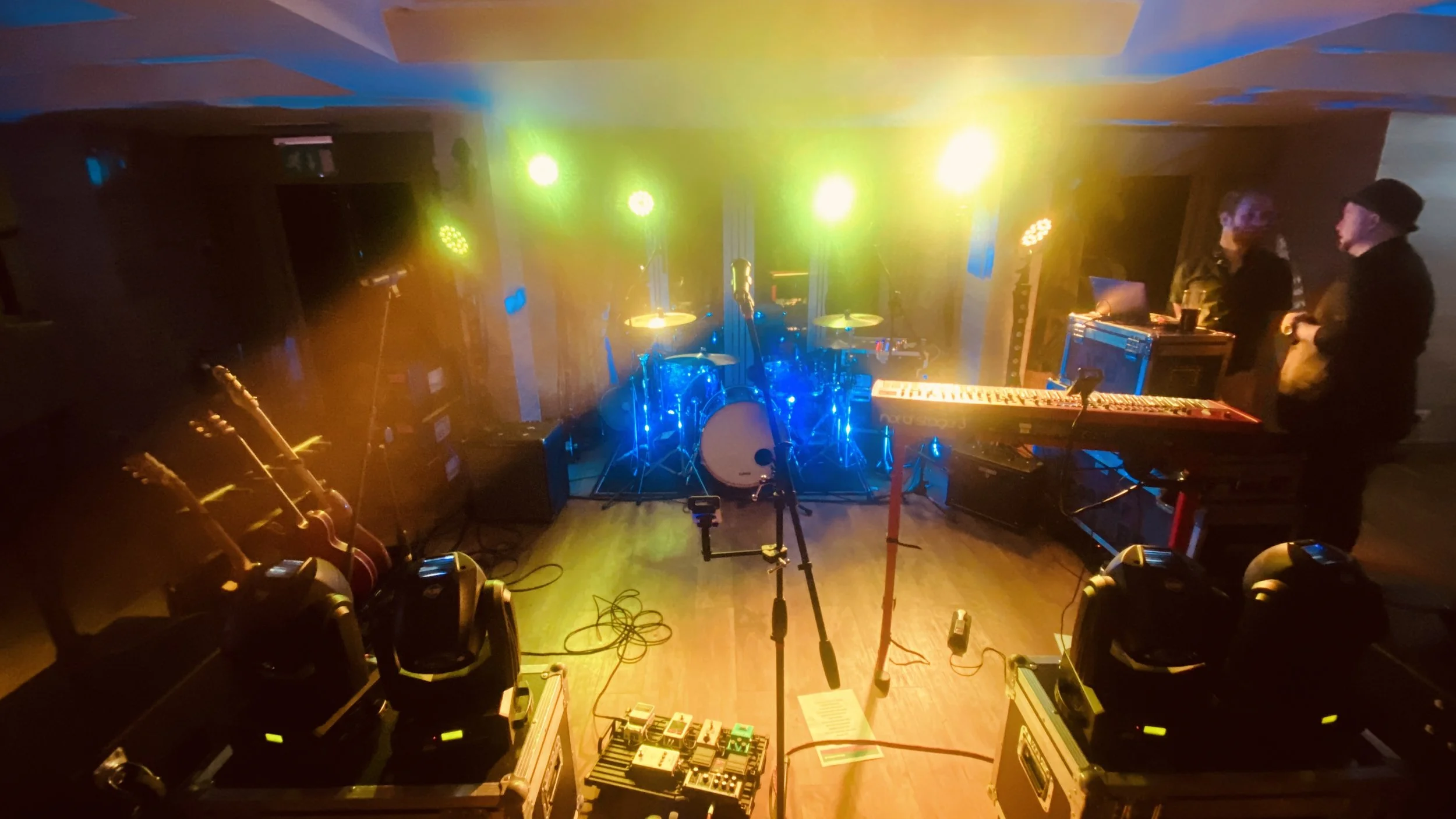 Stage setup with drums, guitars, keyboards, and sound equipment under colorful stage lighting, preparing for a live music performance.