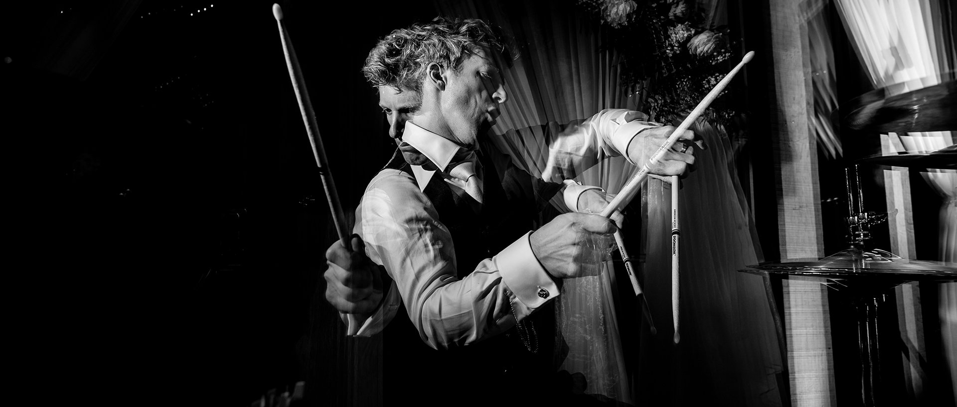 A black-and-white photo of a man dressed as a waiter pouring wine at a party or event.